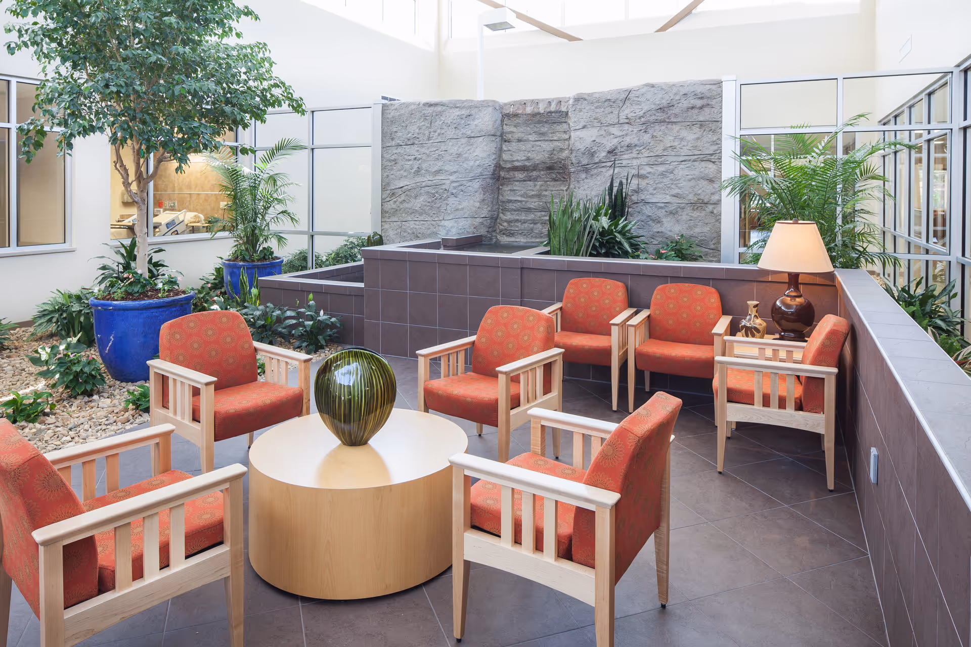 Indoor seating area with red upholstered chairs around a round table in an atrium.