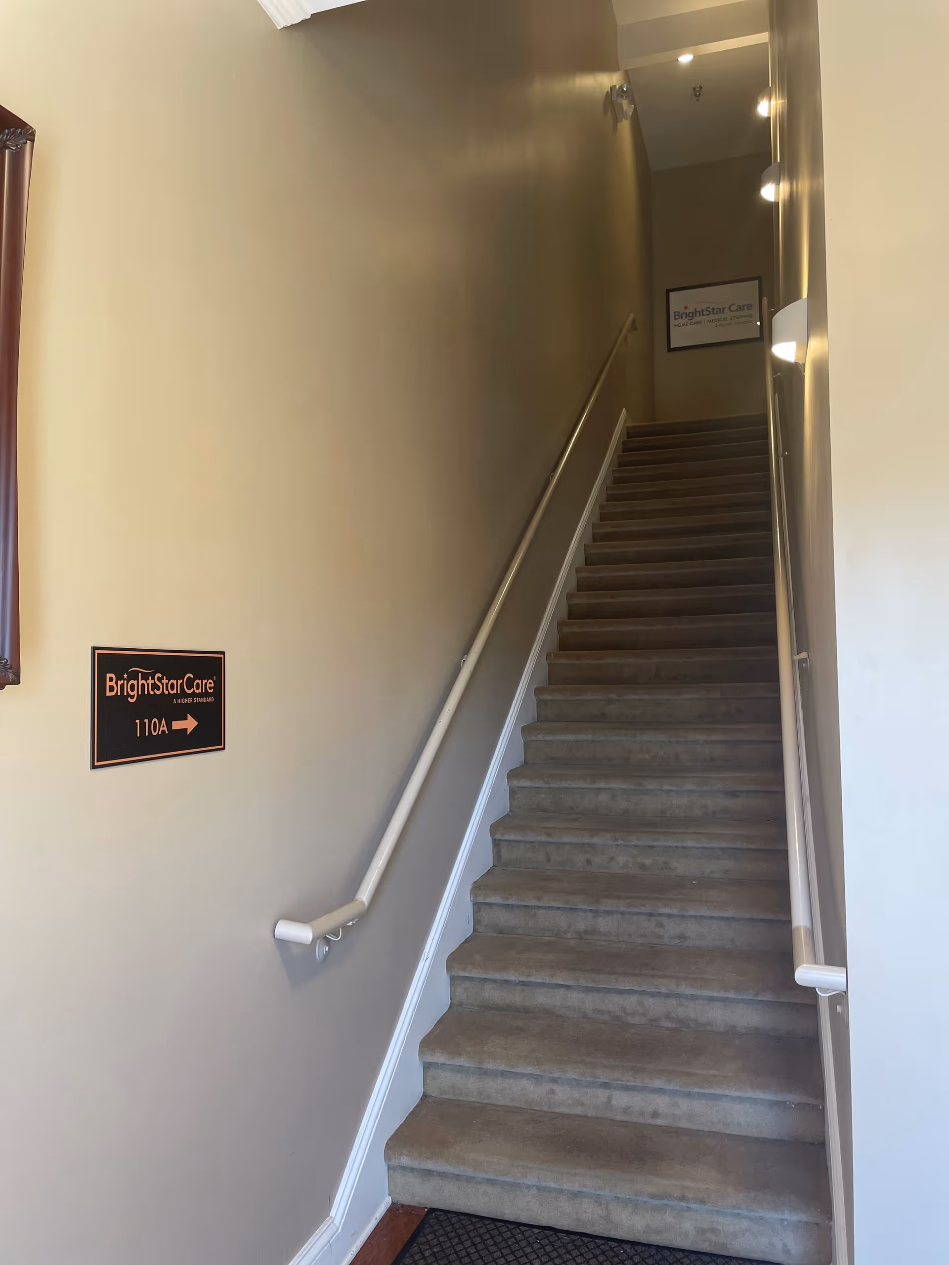 Narrow stairwell in a BrightStar Care facility with beige walls, handrails, and signage.