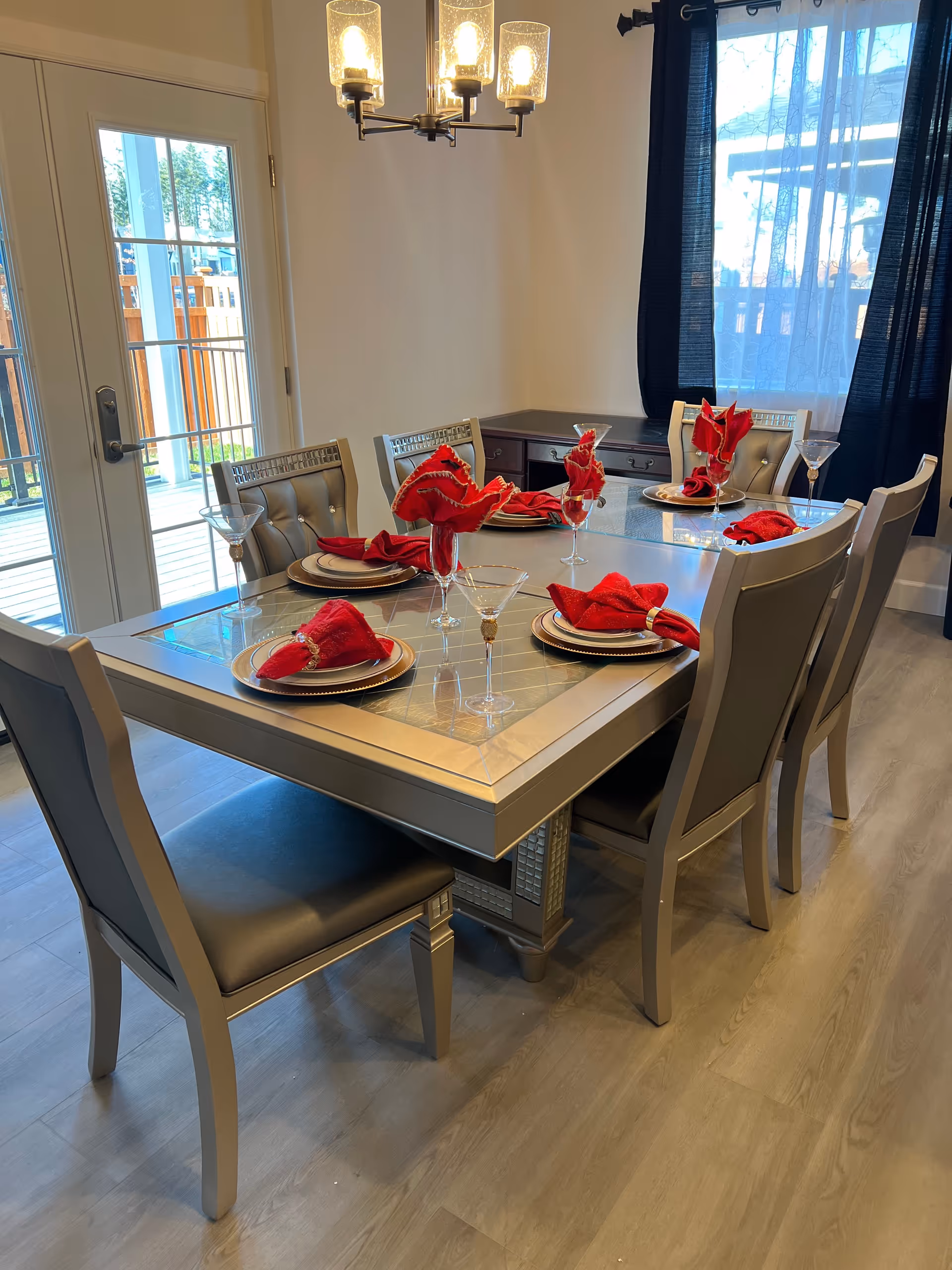 Bright dining room with a glass-top table, six chairs, and red napkin-accented place settings.