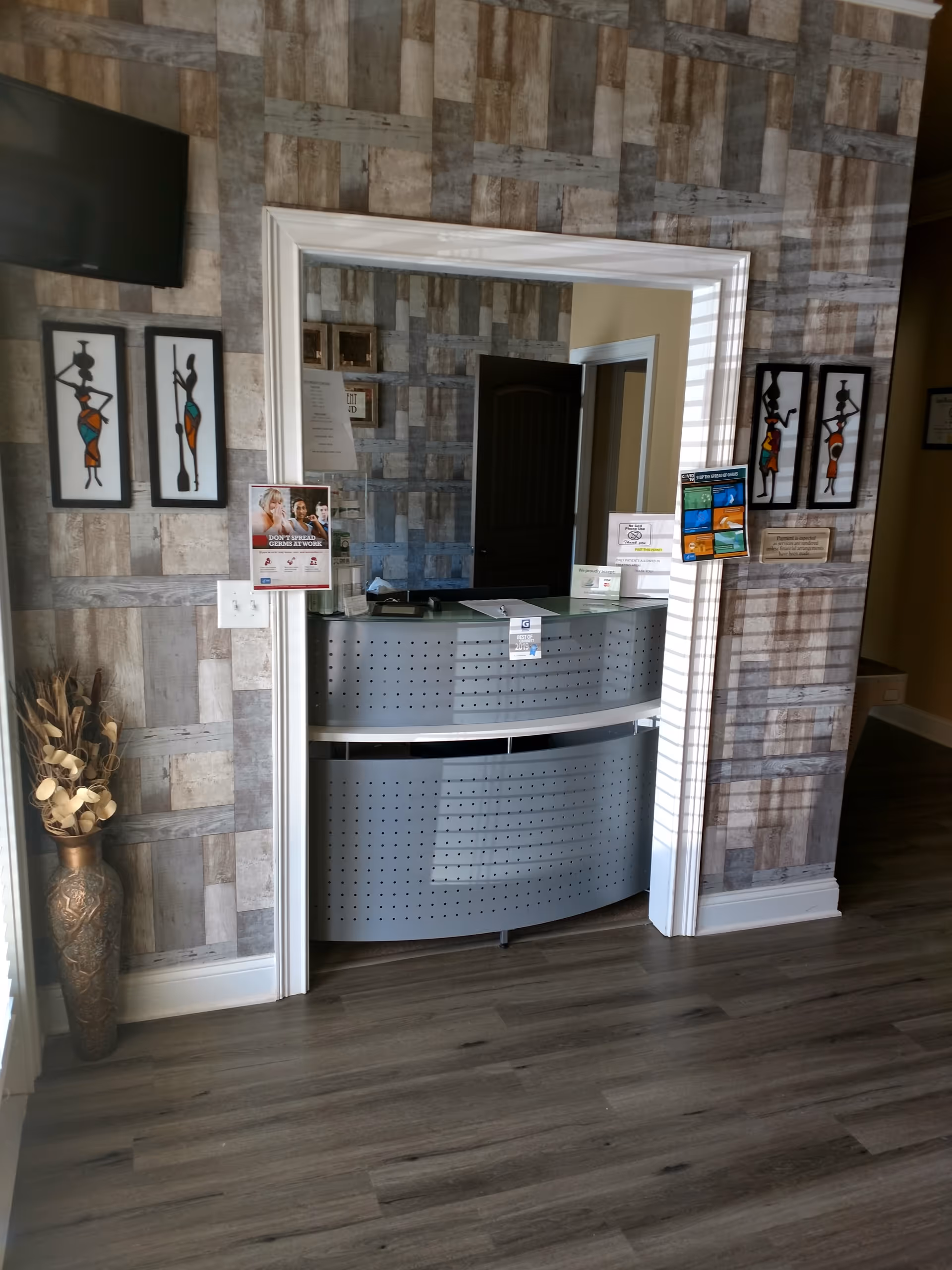 Reception desk in a patterned lobby with wall art, doorway, and a tall vase nearby.