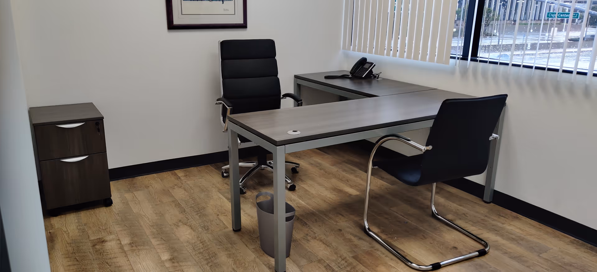 Office workspace with desk, two chairs, filing cabinet, and window blinds.