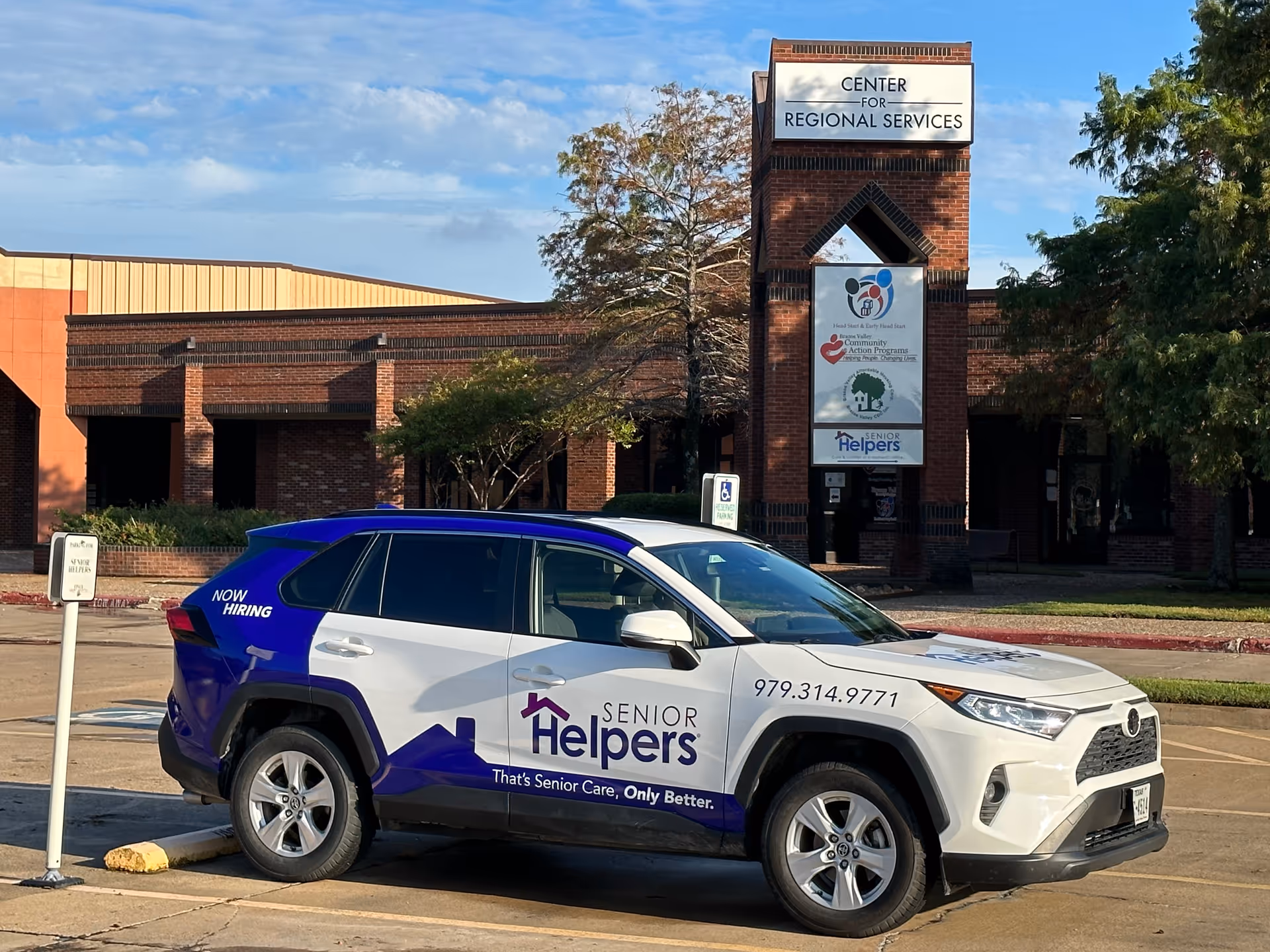 Brick building with a tall sign tower and a Senior Helpers branded SUV parked outside.