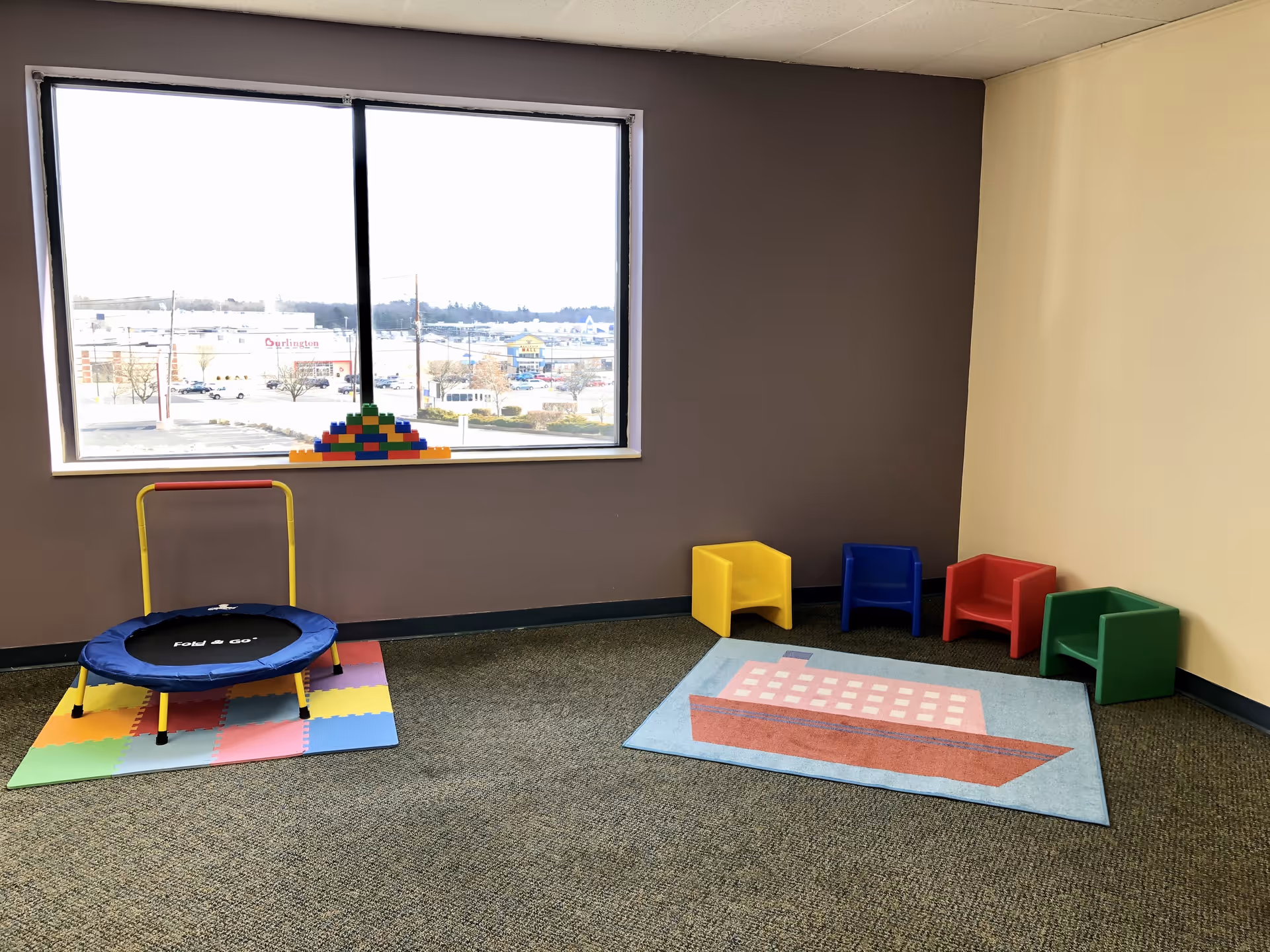 Indoor activity room with a trampoline, colorful seating, and a decorative rug.