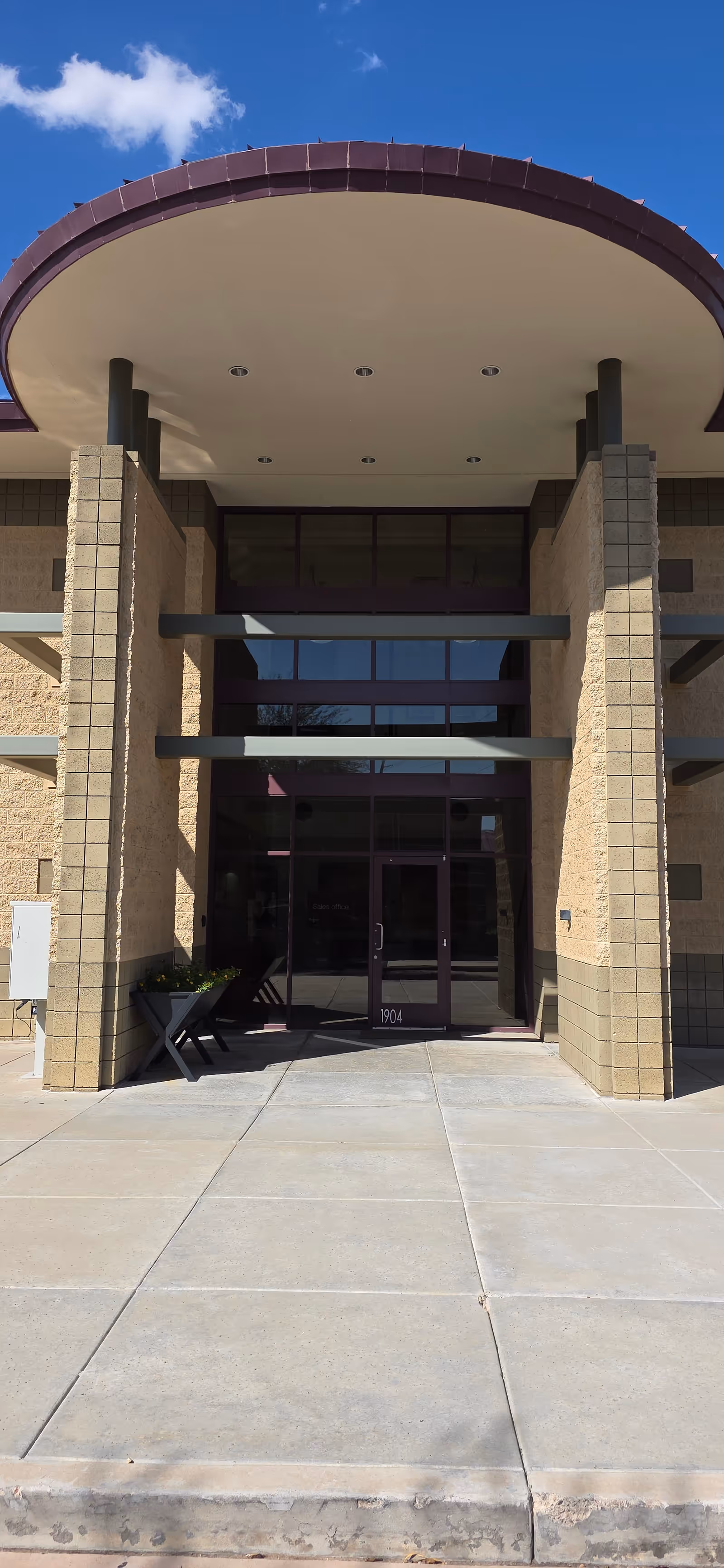 Modern building entrance with glass doors, brick columns, and a curved canopy.