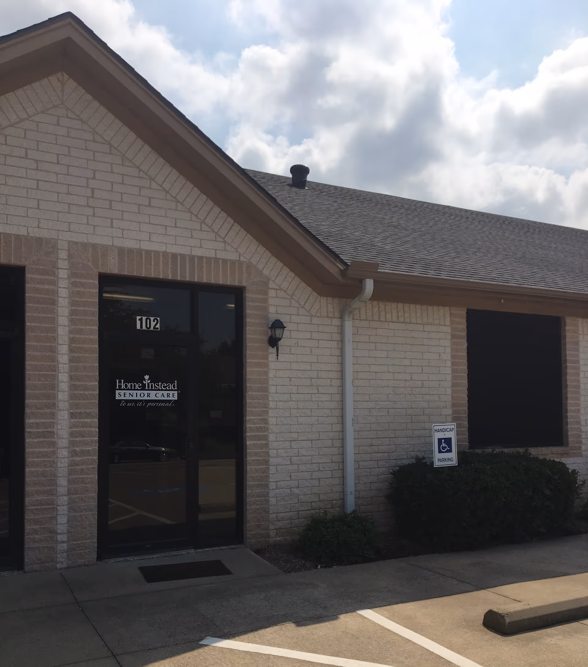Exterior view of a Home Instead building with glass entrance and handicap parking sign.