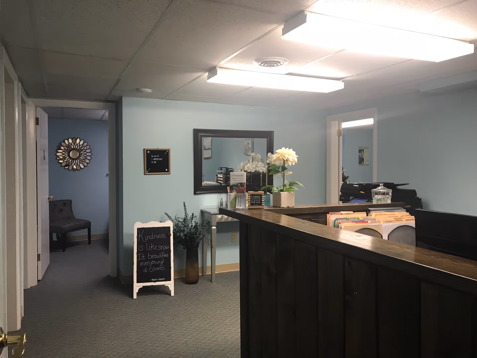Reception area with wooden counter, mirror, plants, and a small chalkboard sign