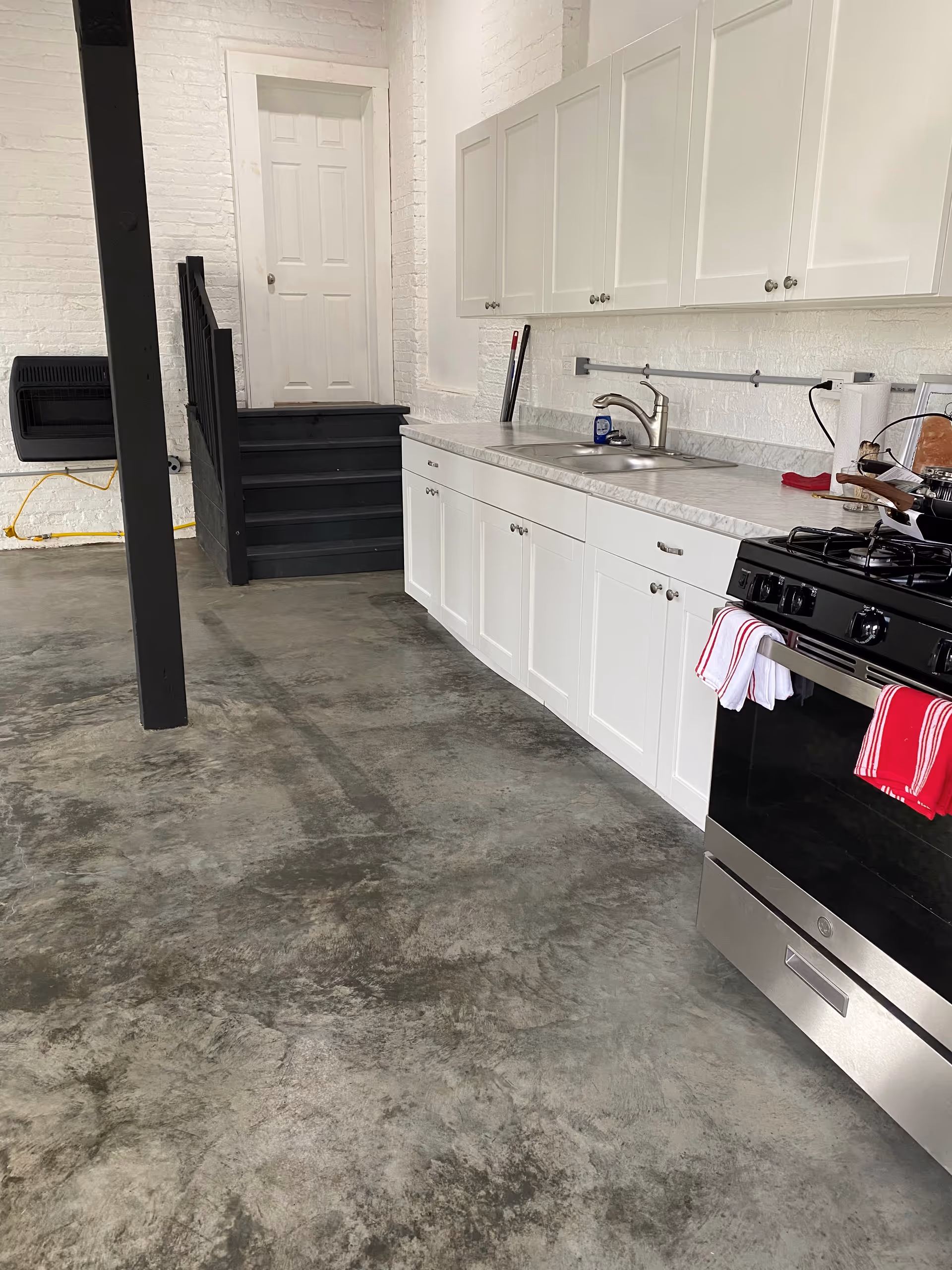 White kitchen area with cabinets, sink, and stove along a concrete floor.