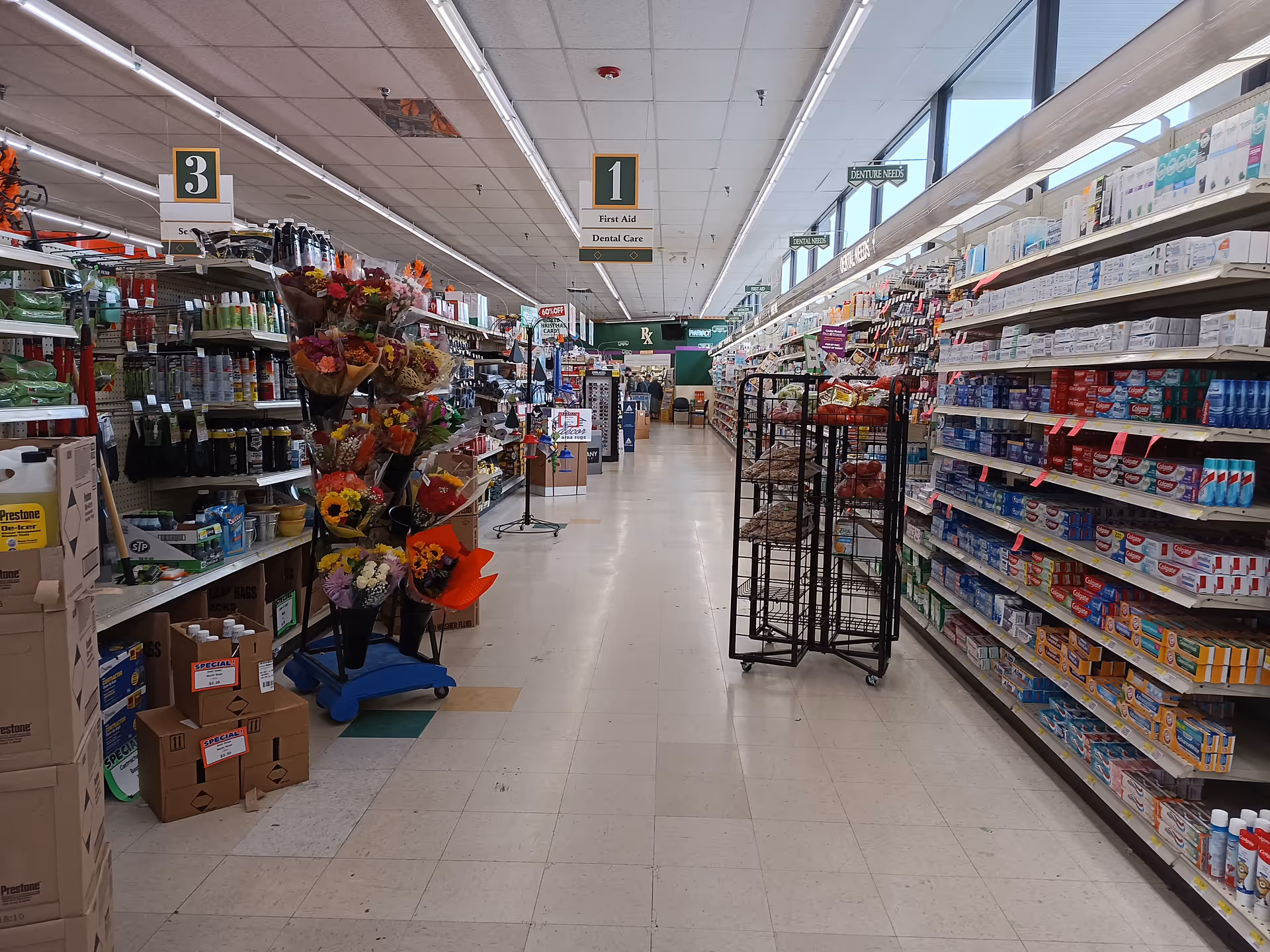 Aisle inside Discount Drug Mart with tall shelves, flowers, and display racks.