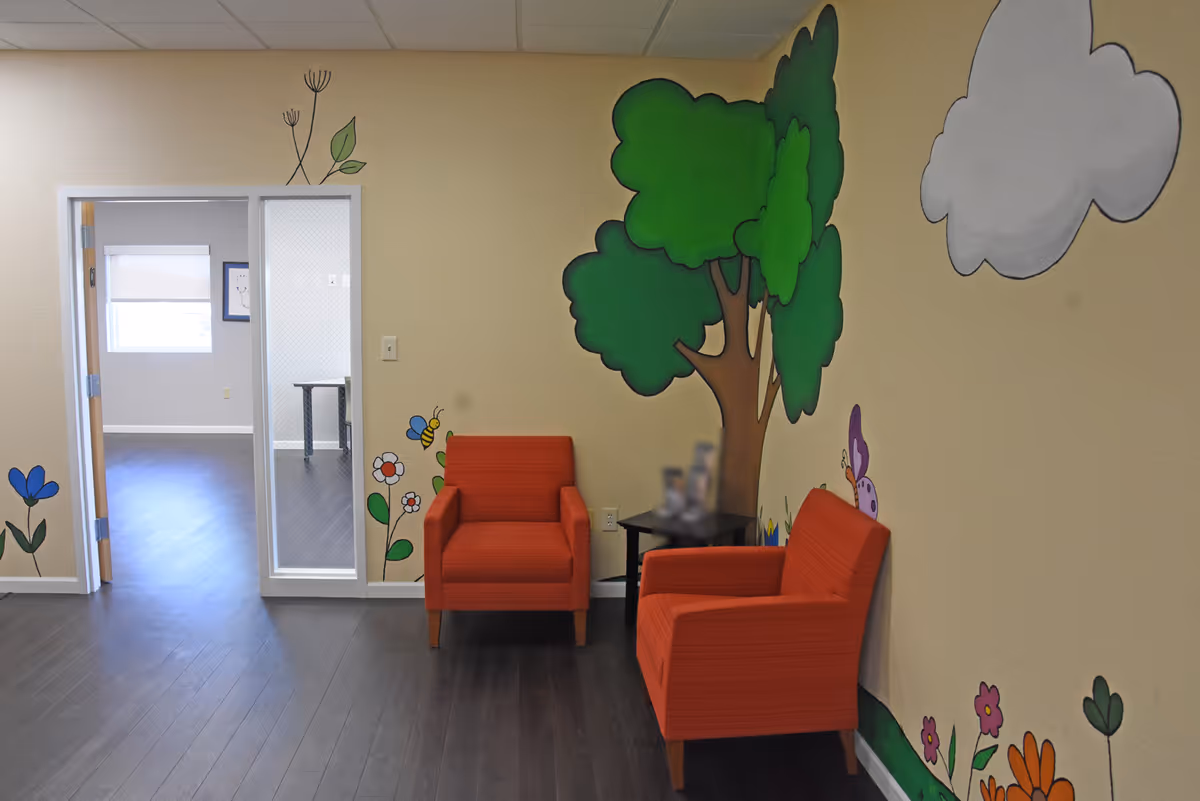 Bright lounge area with orange chairs and wall mural inside a senior living facility.