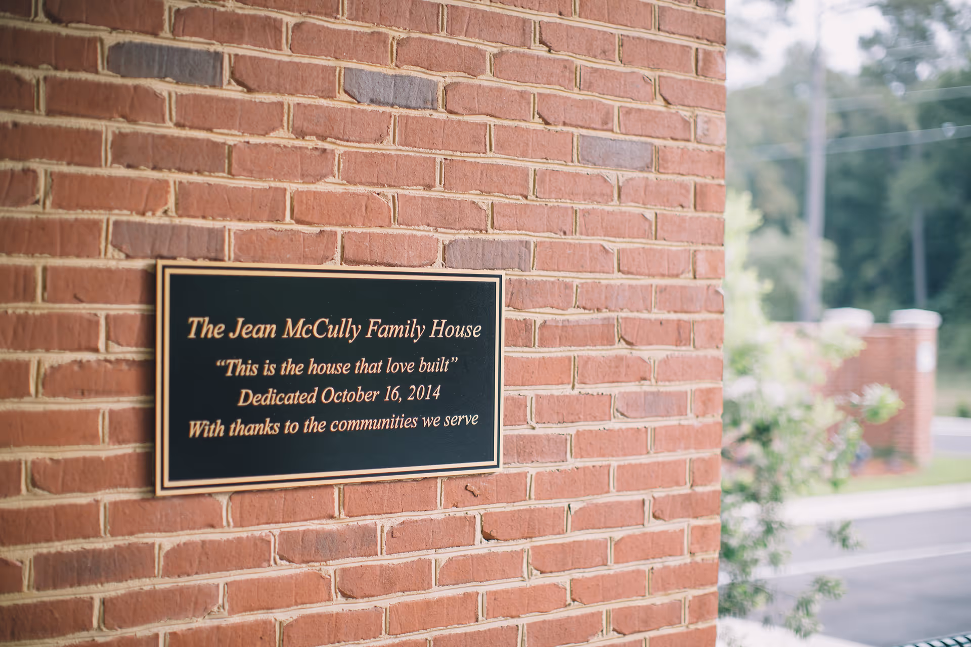 A brick wall with a plaque reading The Jean McCully Family House.