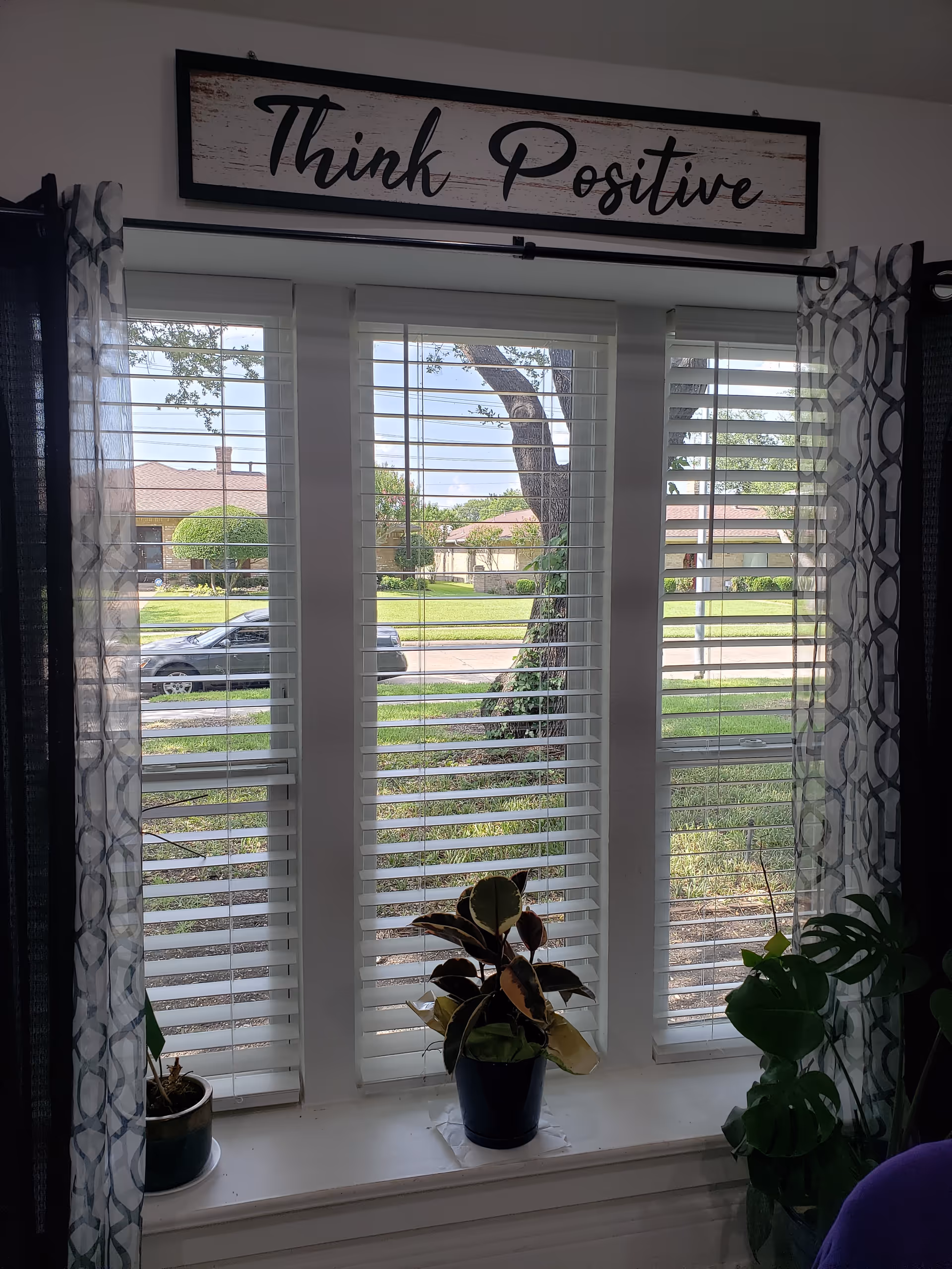 Interior room with window blinds, potted plants, and a Think Positive sign.
