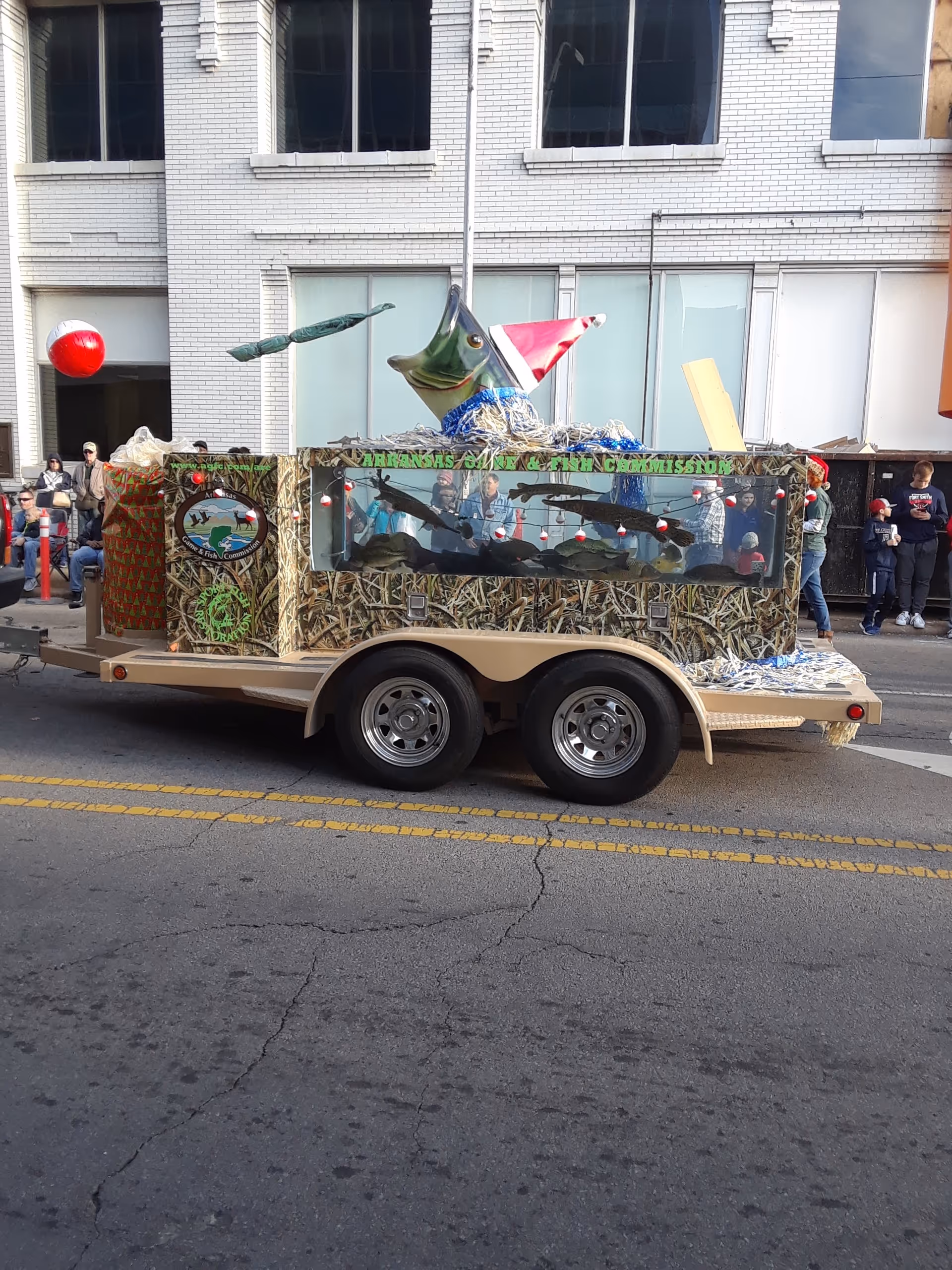 Parade float with camouflage design promoting Area Agency on Aging of Western Arkansas and spectators.