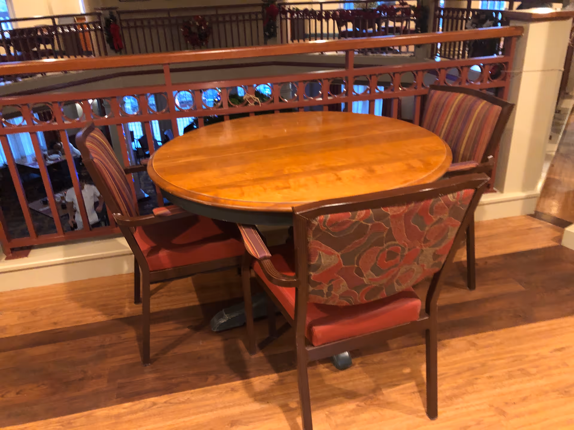 Round wooden dining table with red upholstered chairs in a multi-level senior living dining area.
