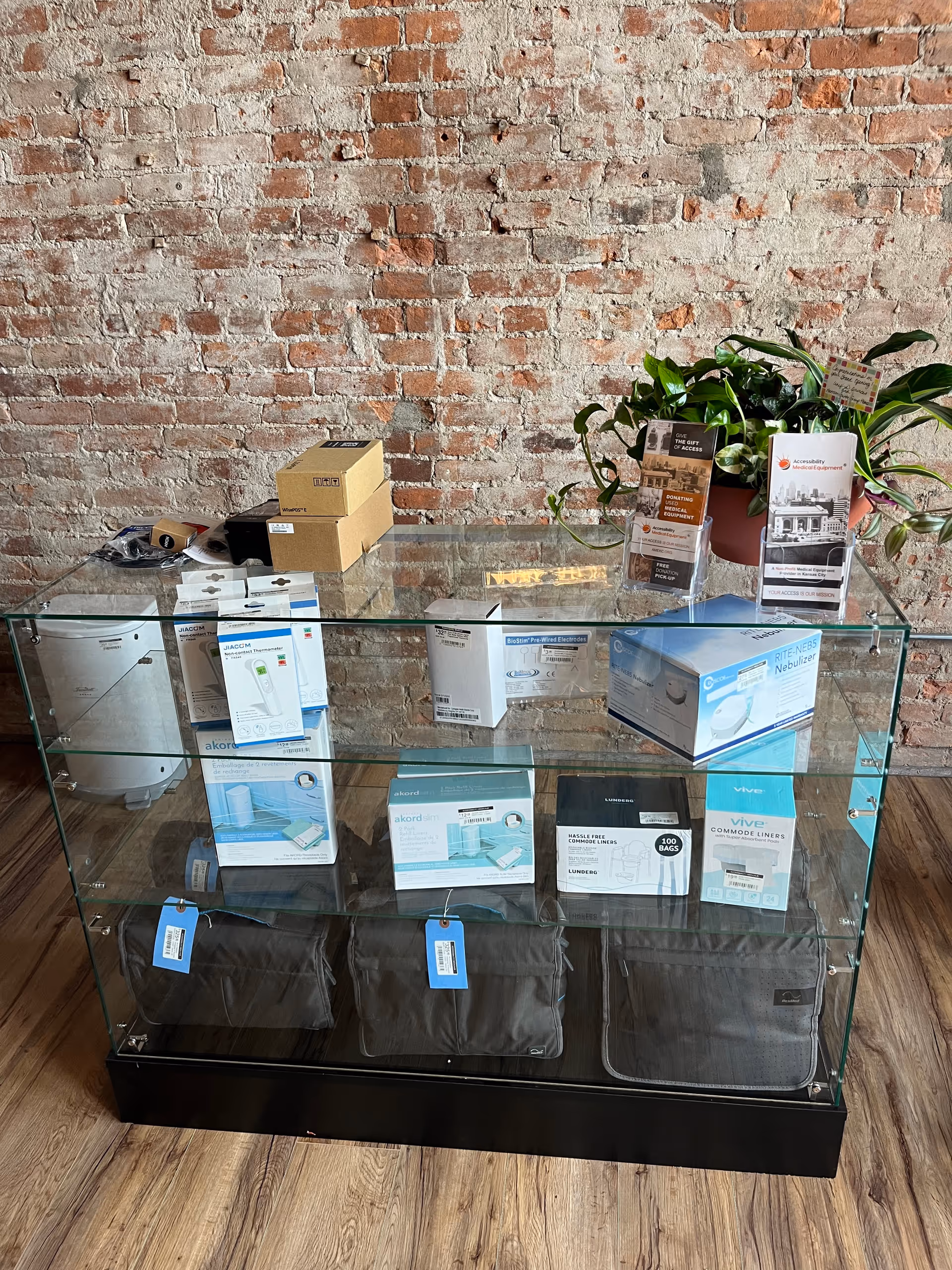 Glass display cabinet filled with boxed supplies, set against a brick wall with a plant.