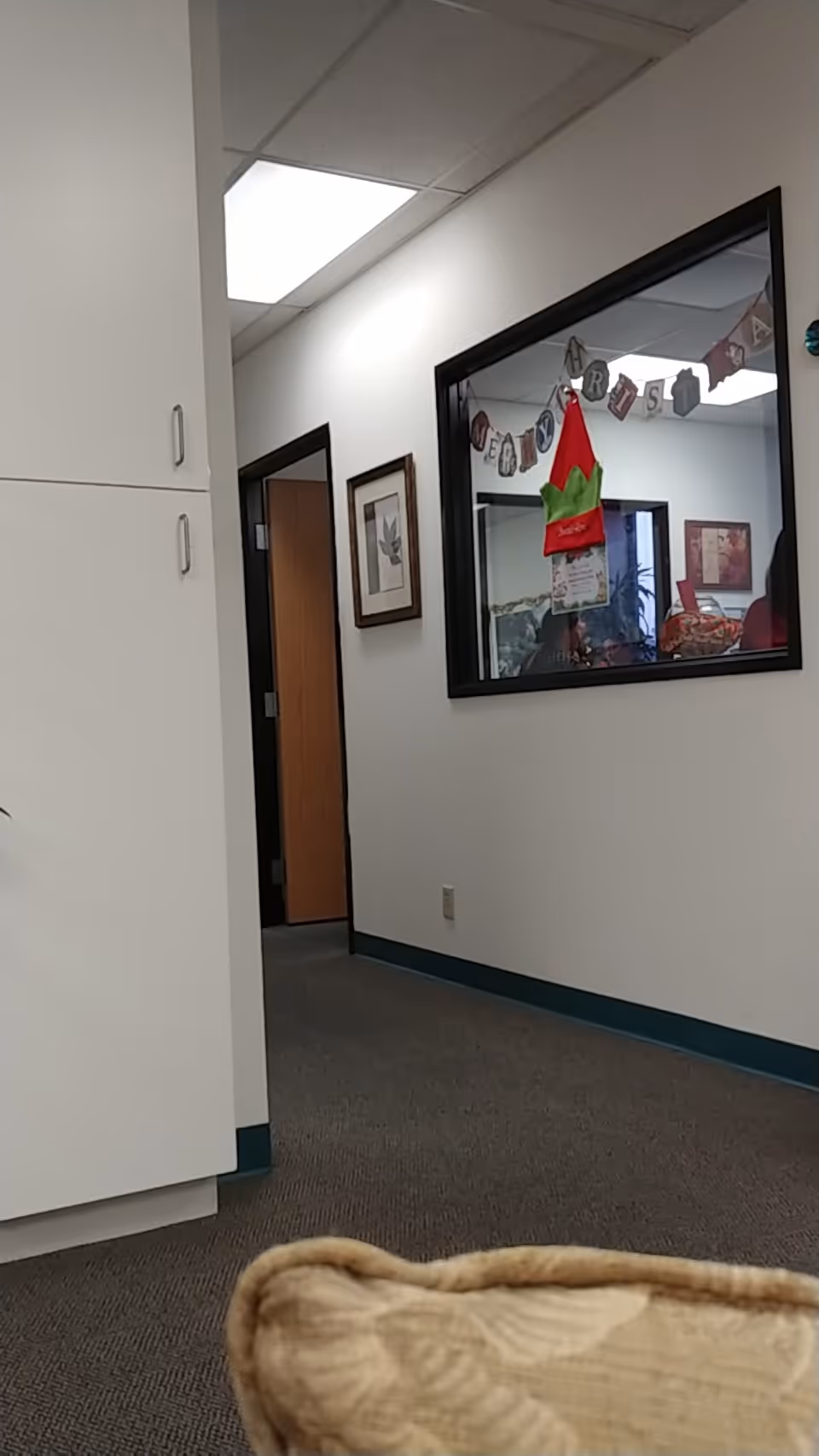 White-walled hallway of a senior facility with cabinets, a holiday banner, and seating area.