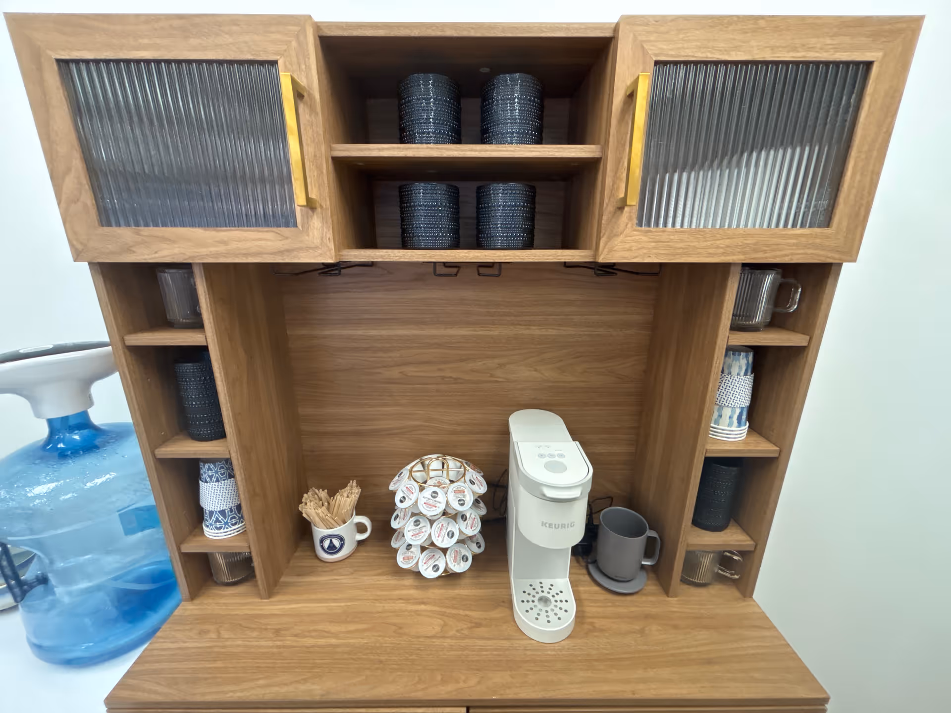 Wooden kitchen coffee station with a Keurig, mugs, and a water dispenser.