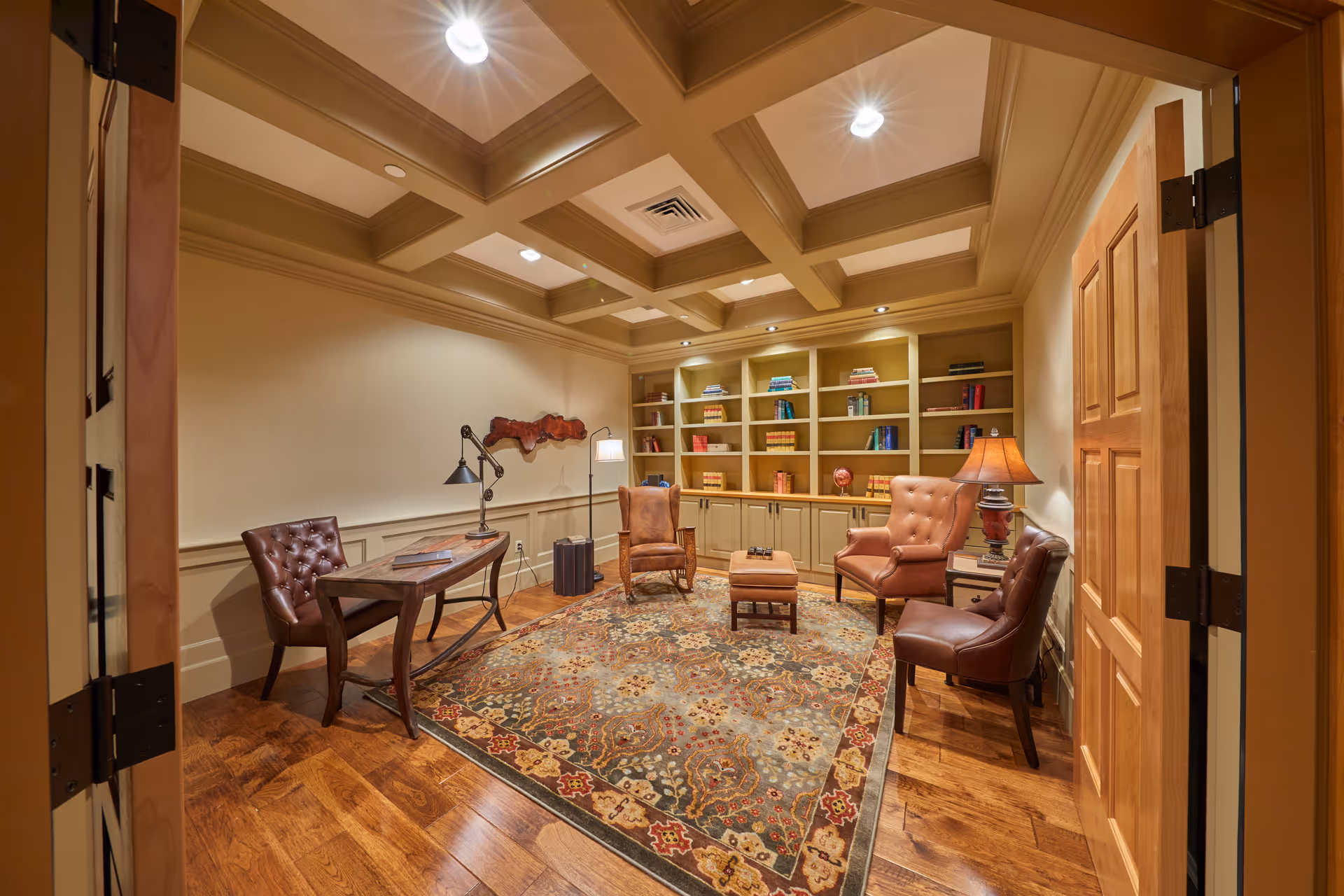Cozy executive-style office/lounge with leather chairs, desk, lamp, rich rug, and built-in bookshelves.