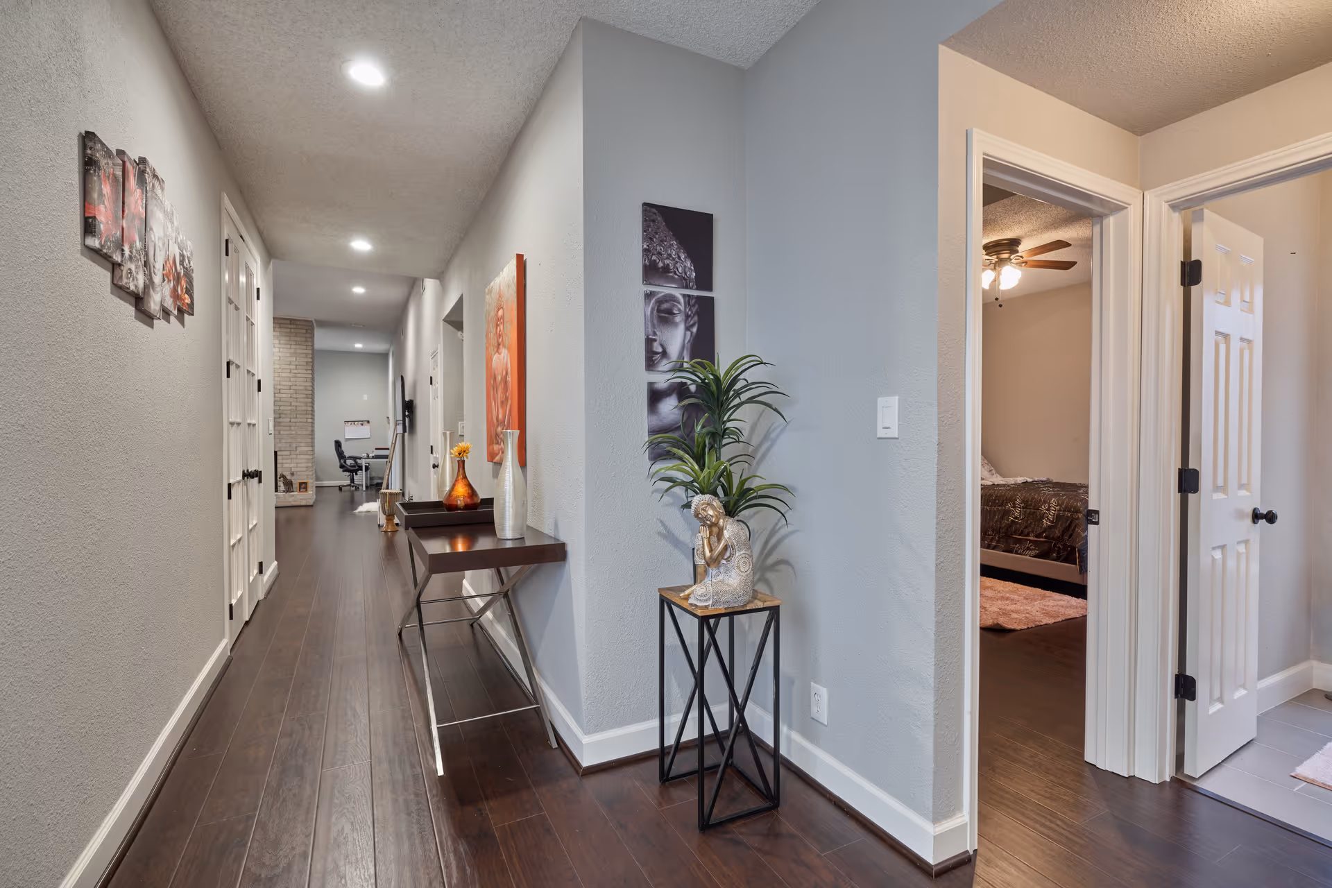 Bright hallway in a senior facility with artwork, a console table, and a doorway to a bedroom.