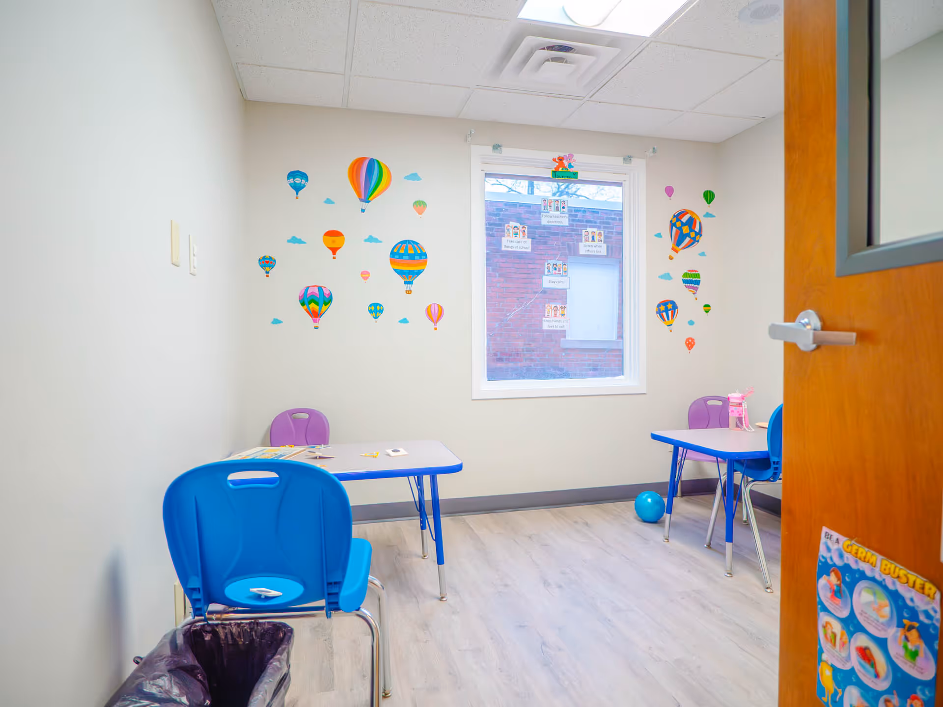 Small bright activity room with blue tables, chairs, and balloon wall decals.