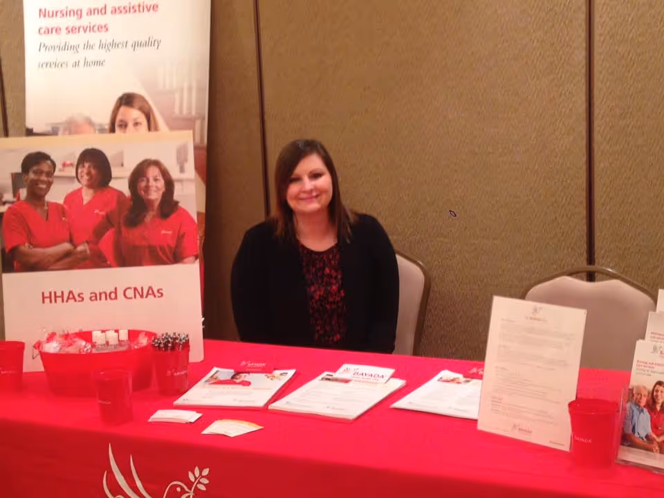 BAYADA Assistive Care booth with a smiling woman seated at a pink table.