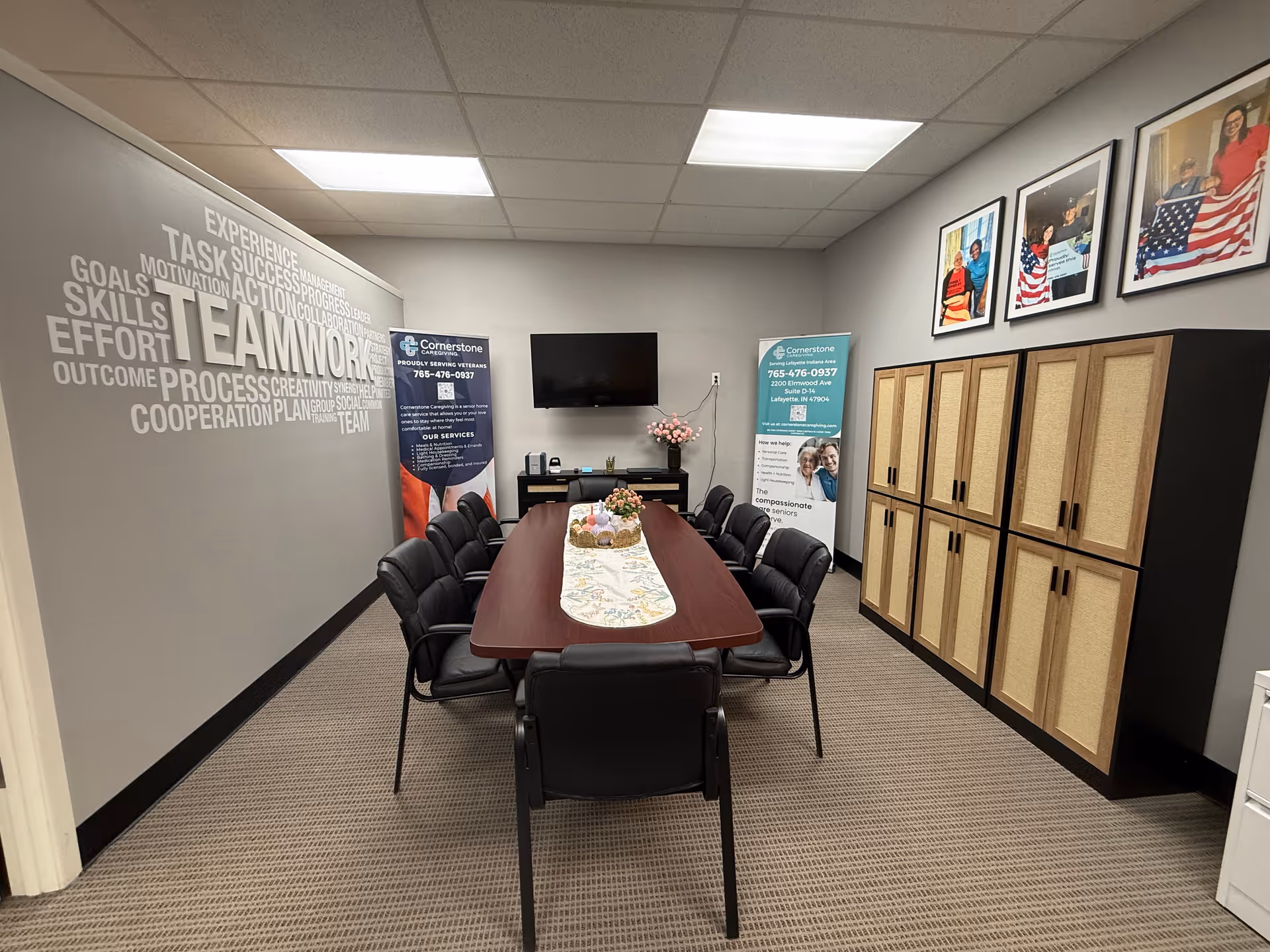 Meeting room with a long table, black chairs, wall word-cloud mural, and cabinets.