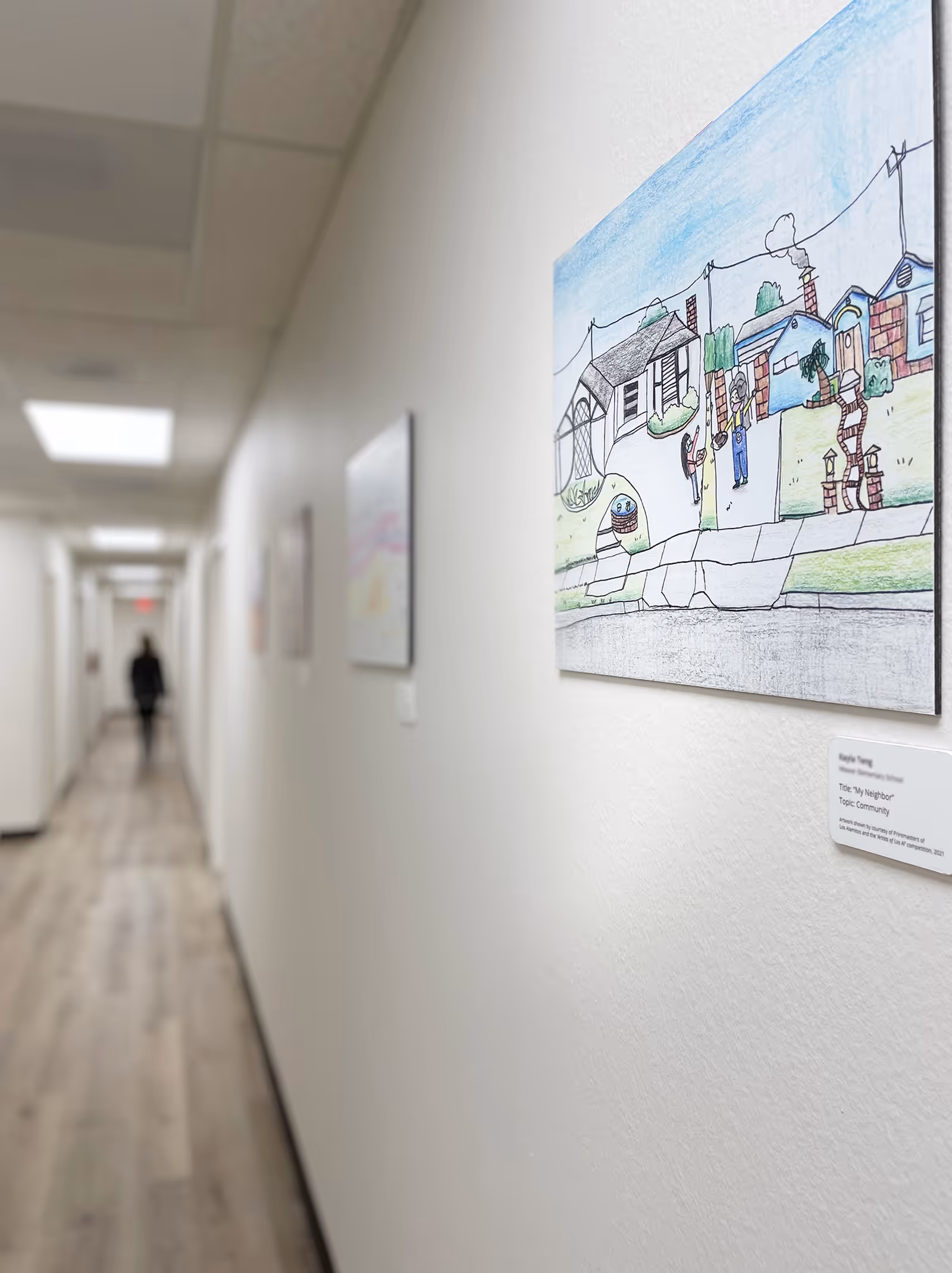Long hallway in a senior care facility with wall art and a distant figure.