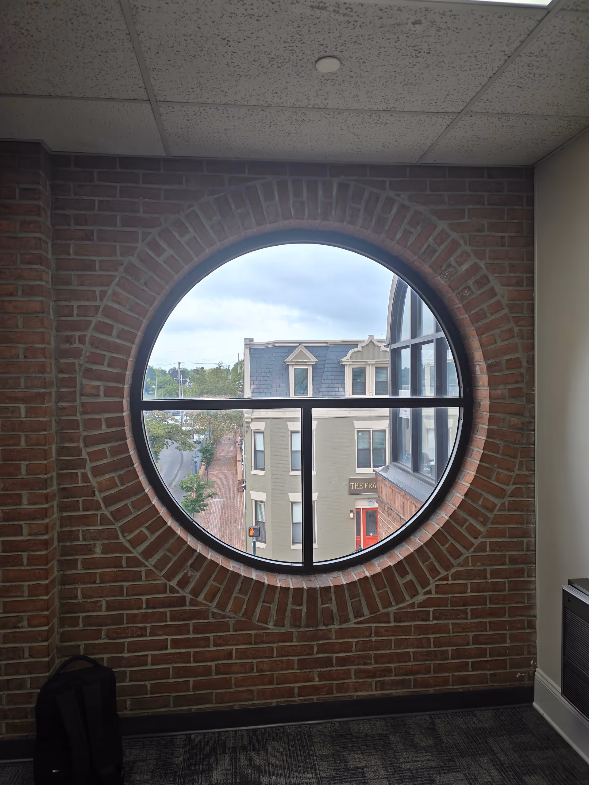 Interior brick hallway with a circular window overlooking a city street.