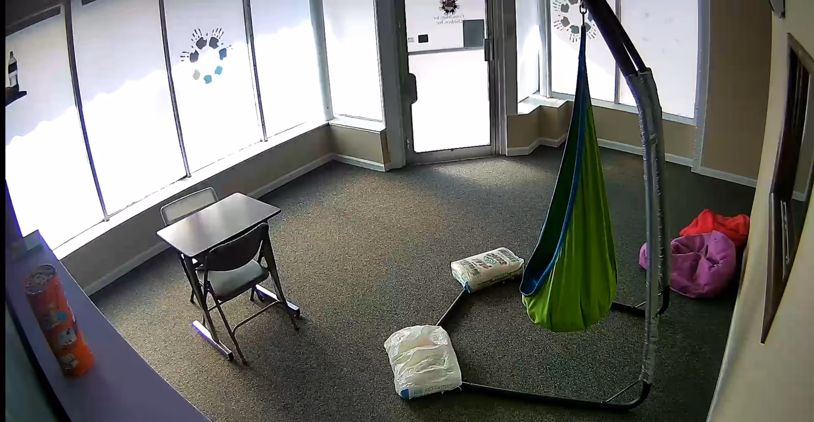 A children's activity room with a hanging green fabric swing, bean bags, and a small desk.