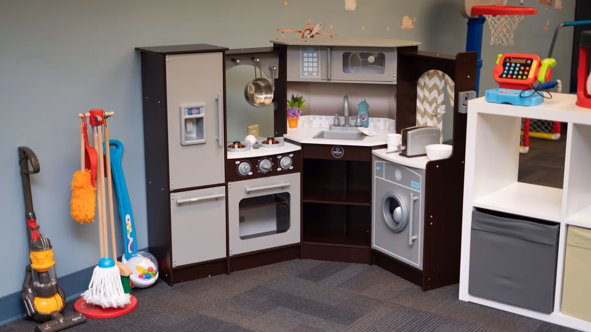 Toy kitchen setup with appliances and cleaning tools in a playroom