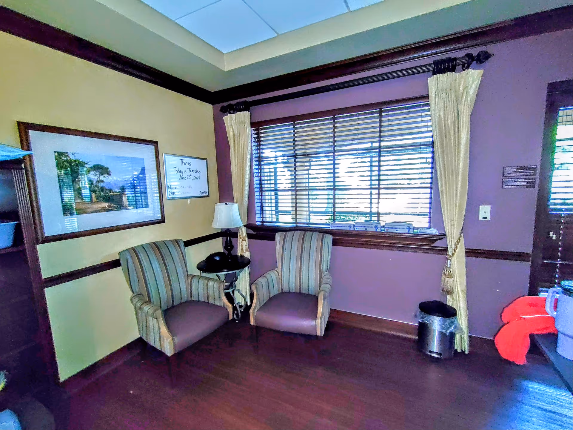 Cozy indoor lounge with two striped armchairs, a small table lamp, and a large window.