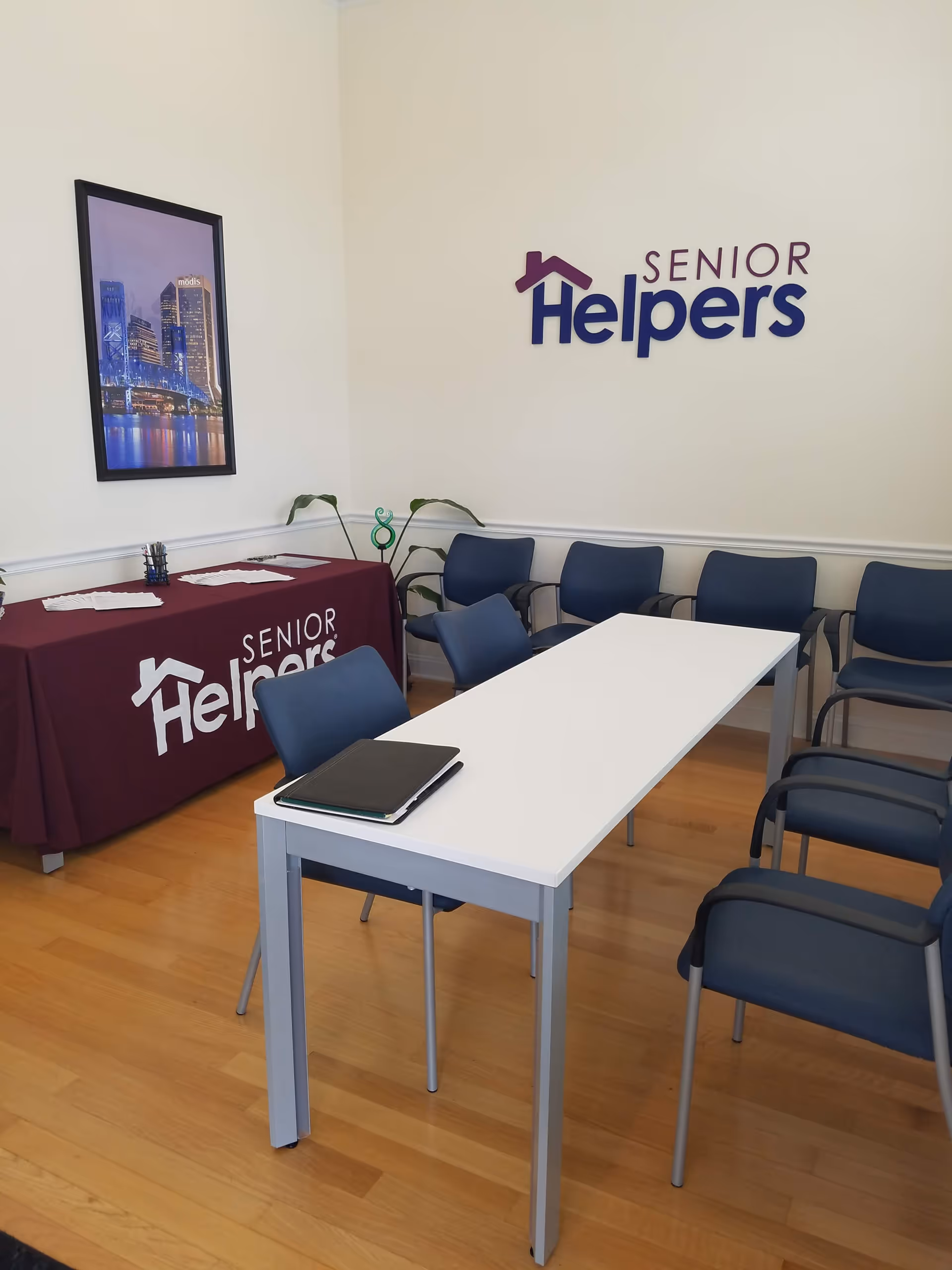 A meeting room with a long white table, blue chairs, and Senior Helpers branding.
