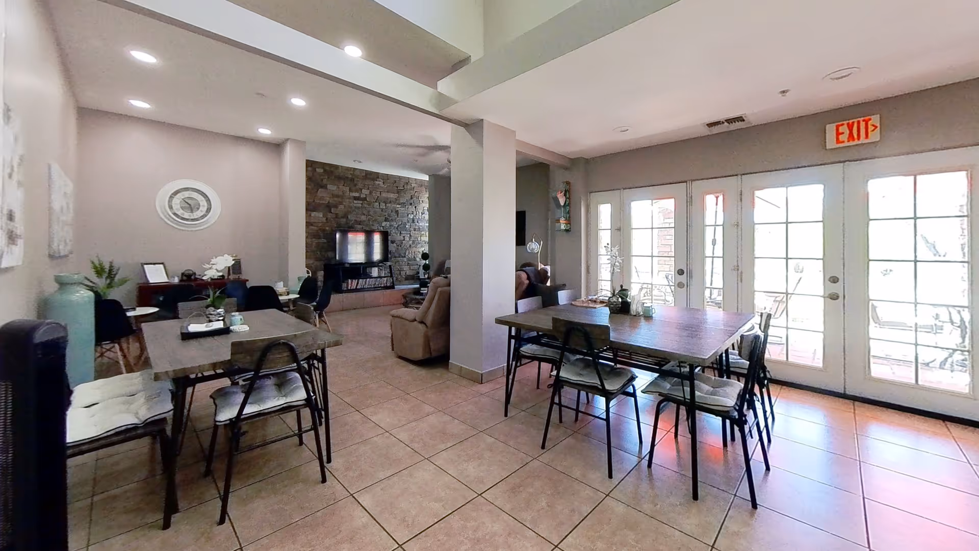 Bright dining area in a senior living facility with tables, chairs, and a stone wall.