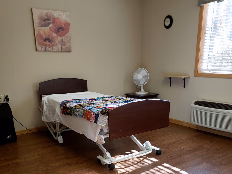 A single residential bedroom with a bed, quilt, fan, and window.