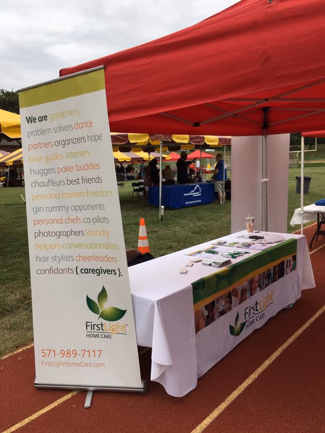 Outdoor FirstLight Home Care booth with banner and table at event.