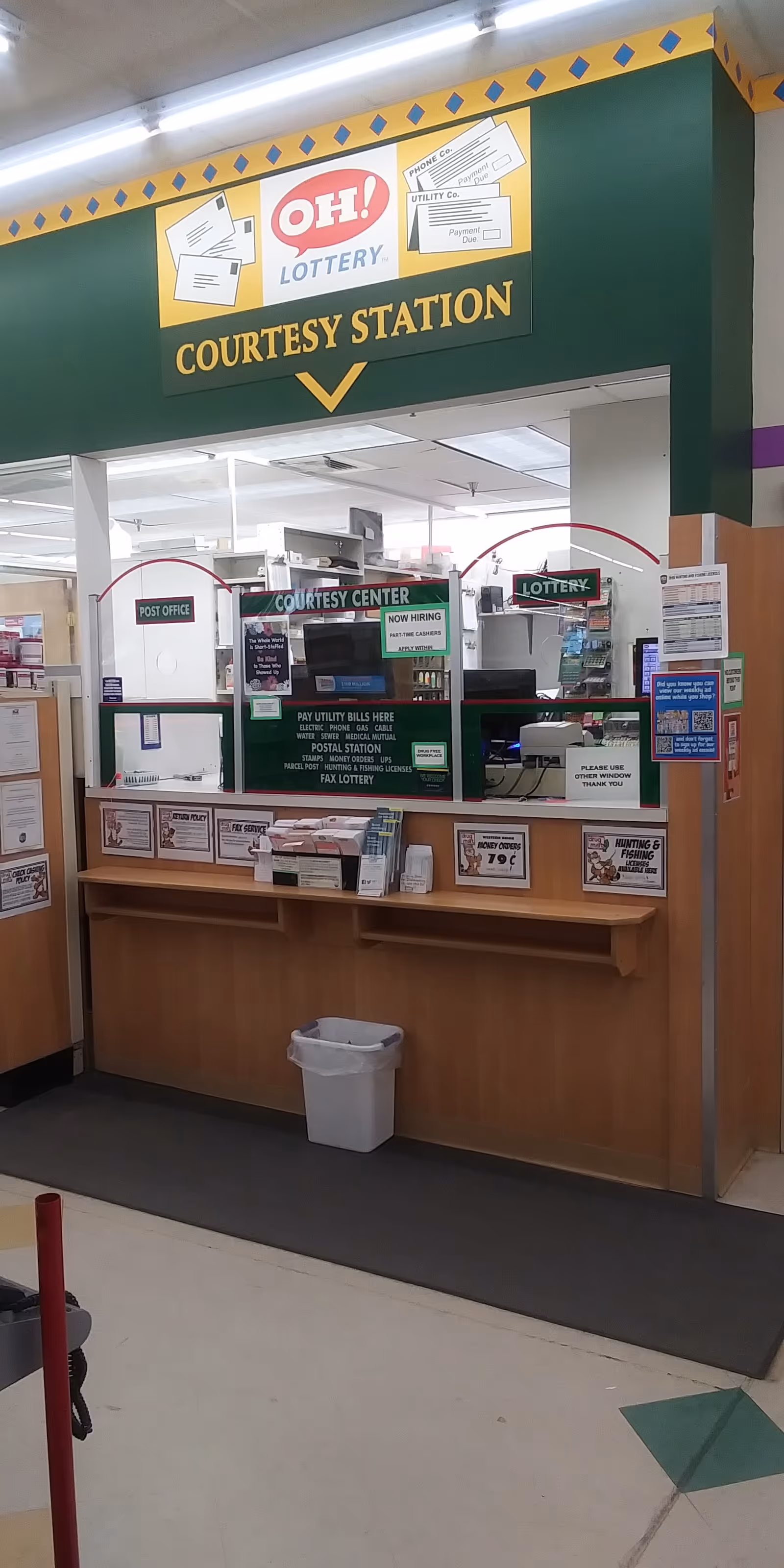 Indoor service counter labeled Courtesy Station with lottery and post office windows.