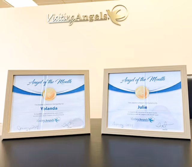 Two framed awards sit on a dark surface beneath the Visiting Angels sign.