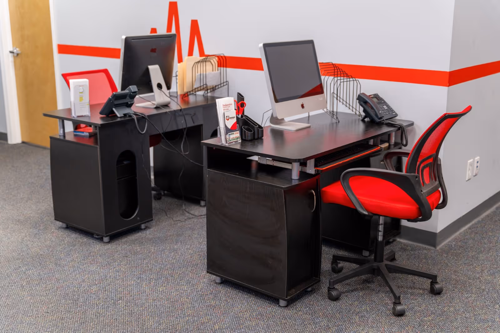 Two desks with computer monitors and a red office chair in a modern interior.