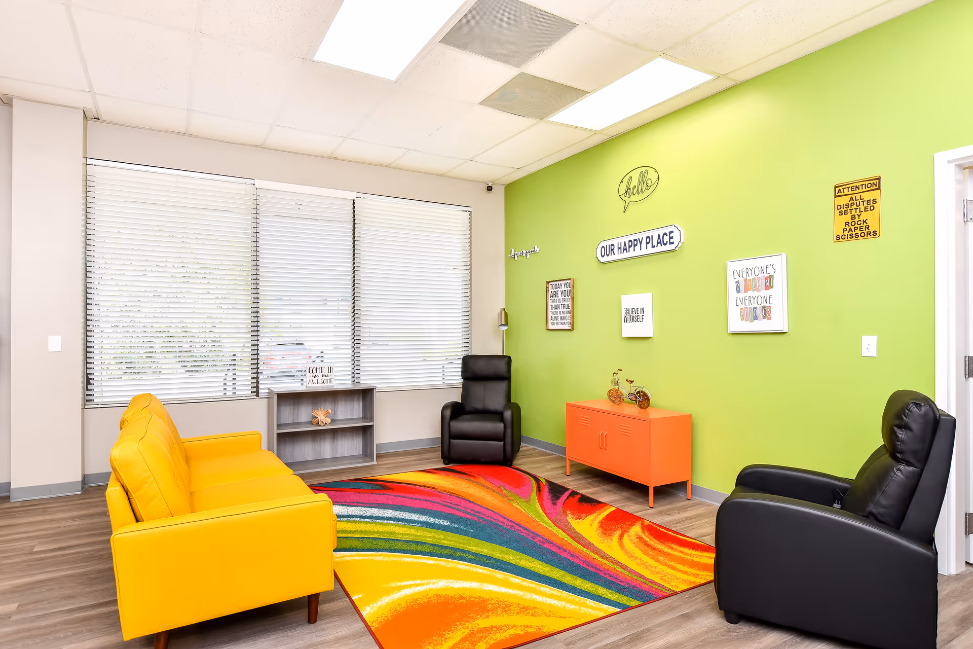 Bright senior living lounge with lime-green wall, colorful rug, and yellow and black chairs.