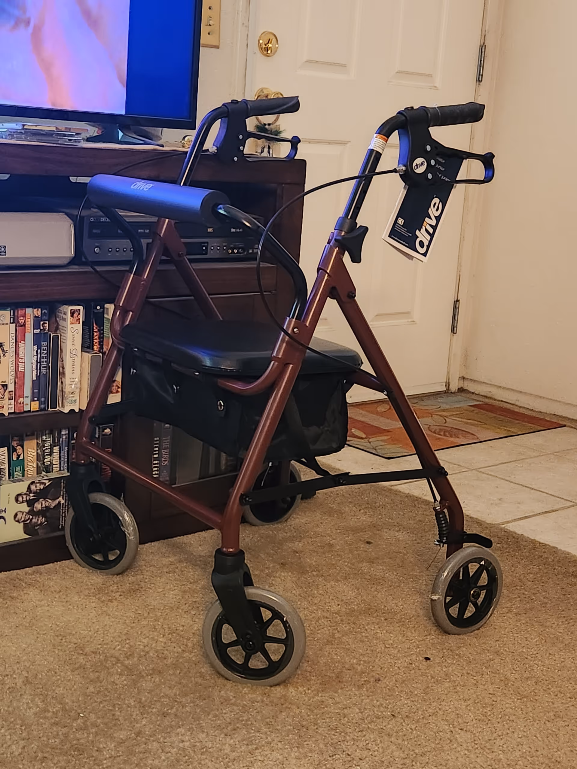 Maroon rollator walker with seat rests inside a living room near TV.