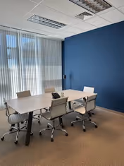 Modern meeting room with a white table, chairs, blue wall, and large windows