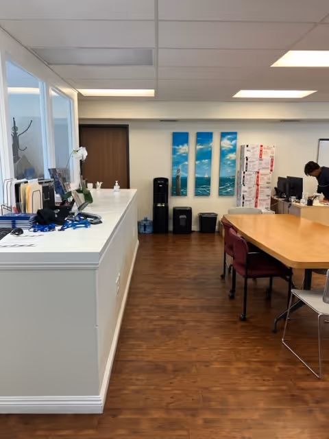 Reception area with white counter, wooden floor, long table, and staff at a desk