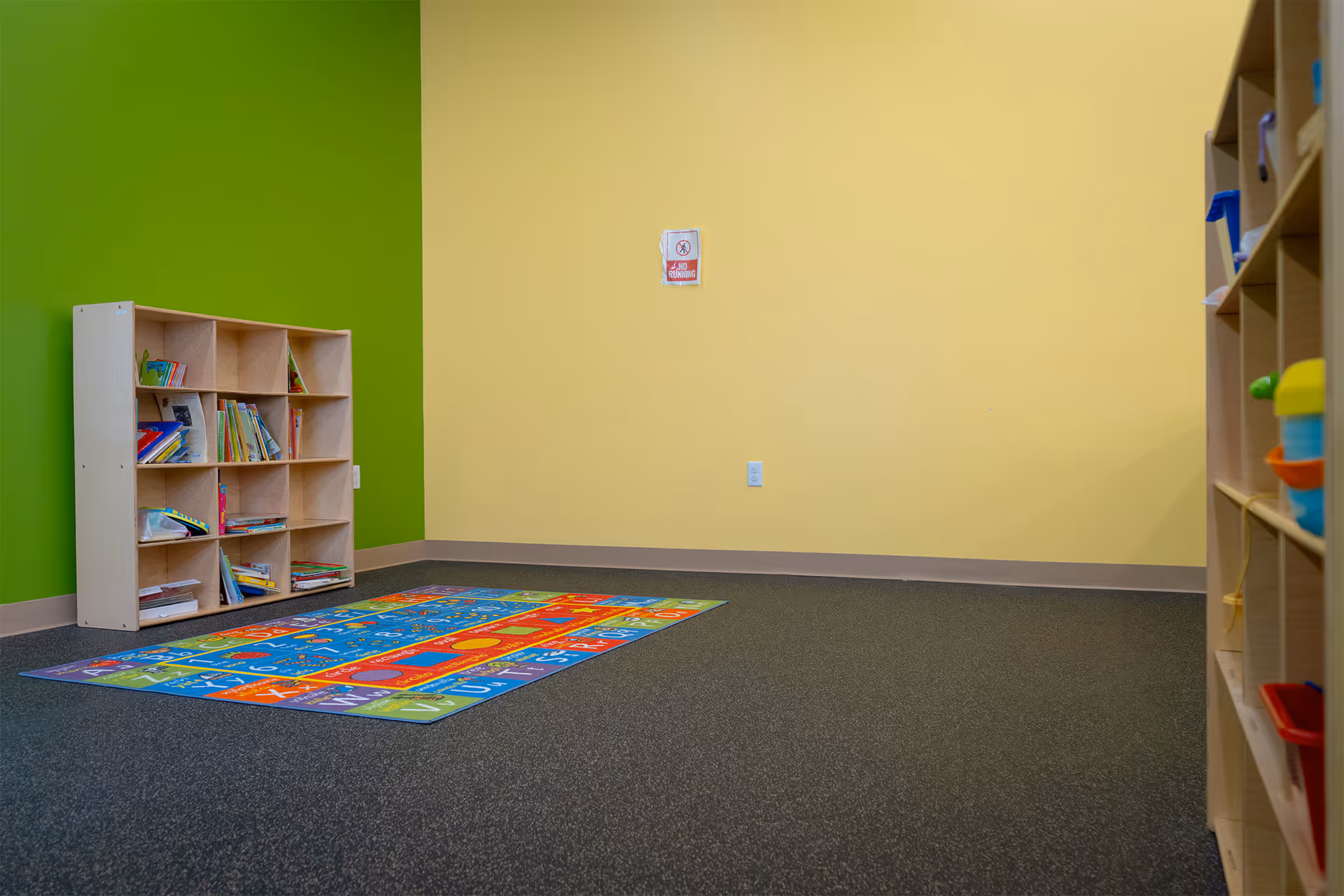 Bright playroom with green and yellow walls, shelves, and a colorful carpet.