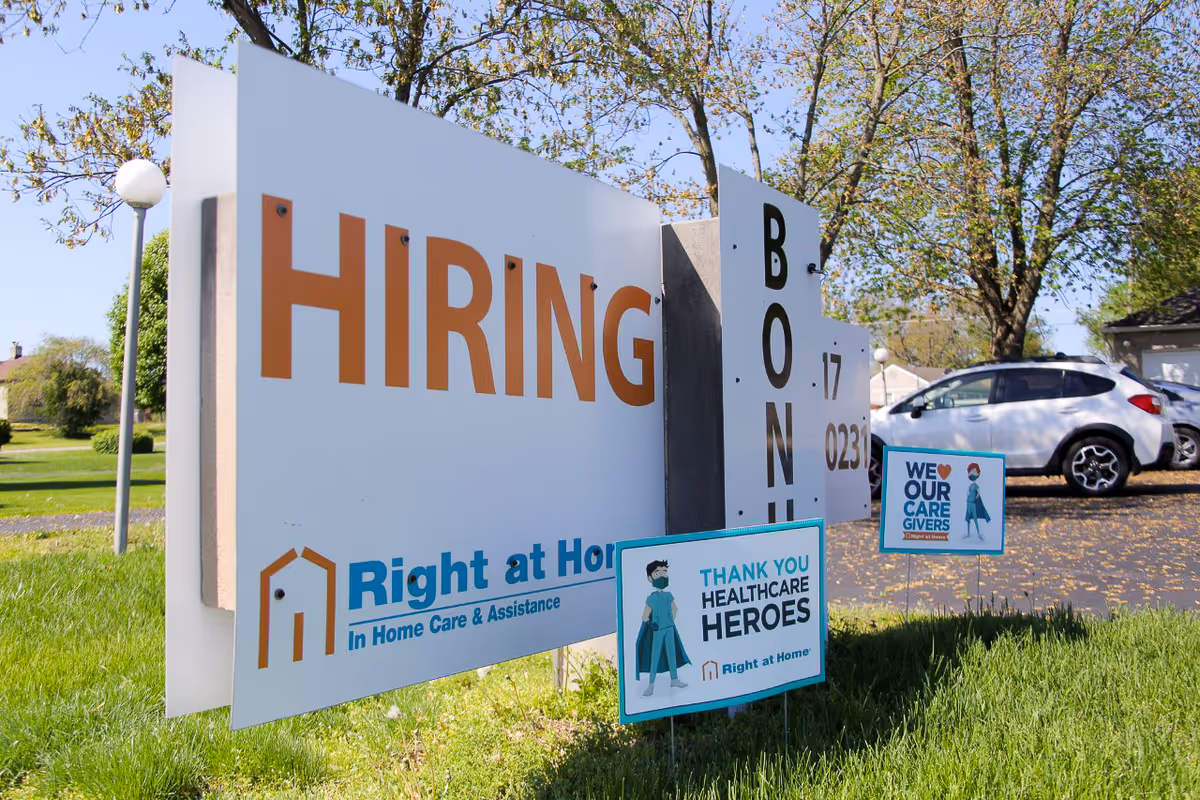 Outdoor sign reads HIRING for Right at Home, with a car in the parking lot.