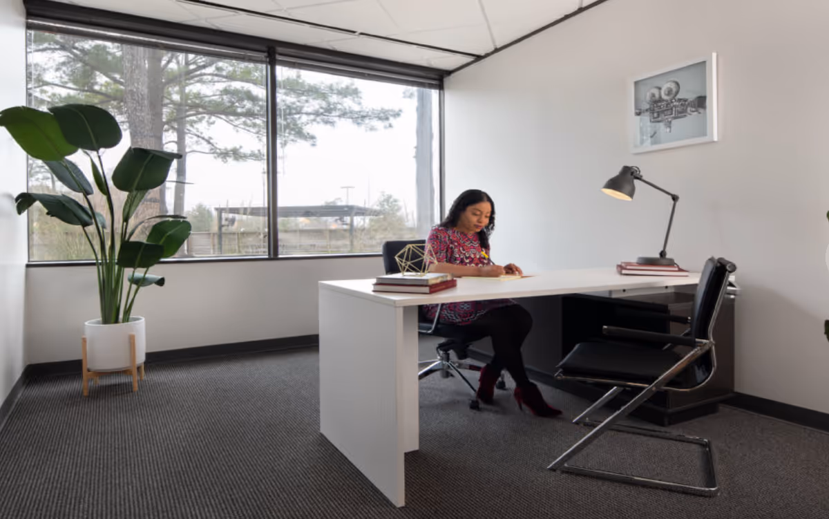 A woman sits at a white desk in a bright, modern office space.
