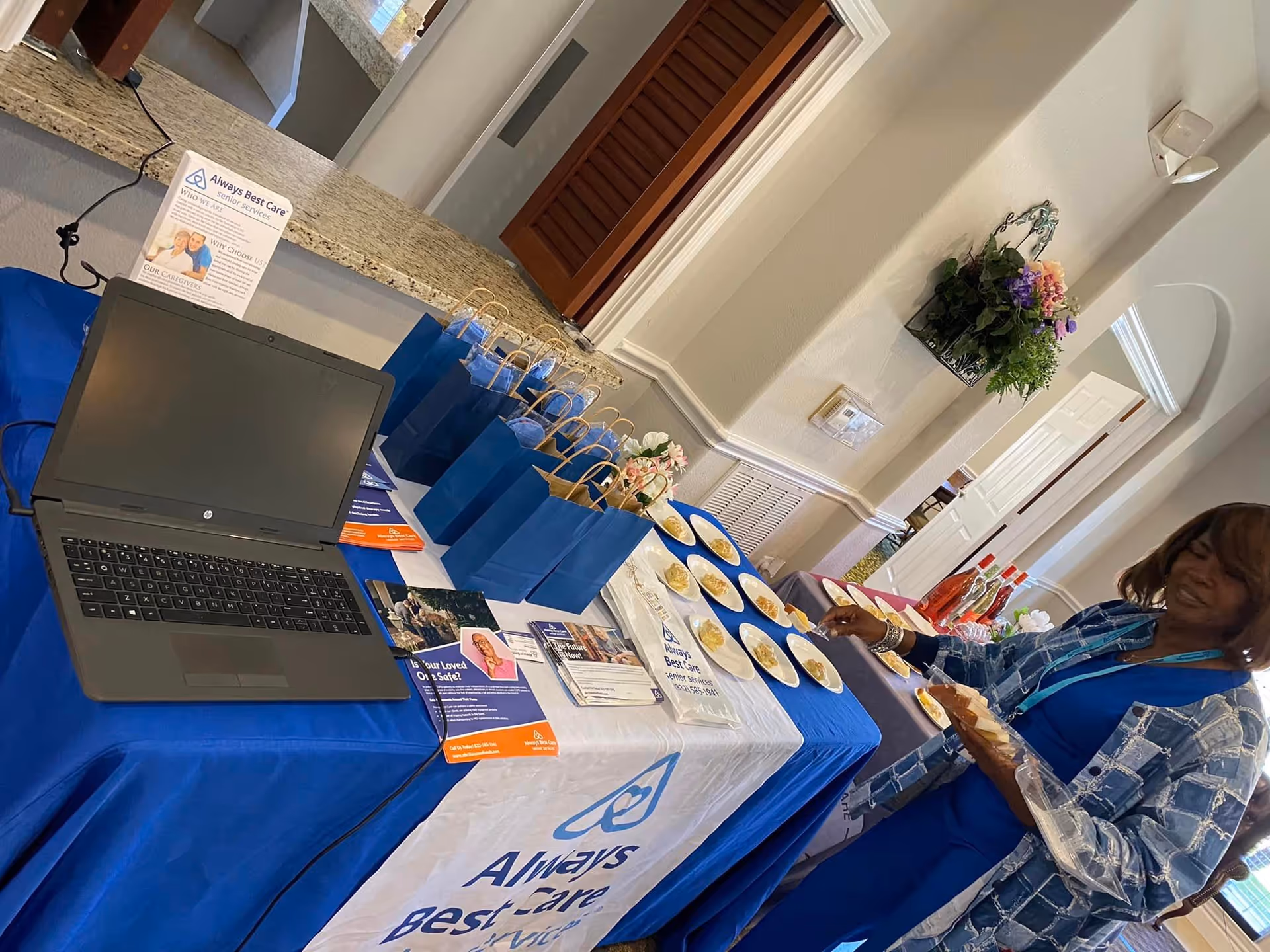 Promotional table with blue tablecloth, laptop, brochures, and a staff member indoors.