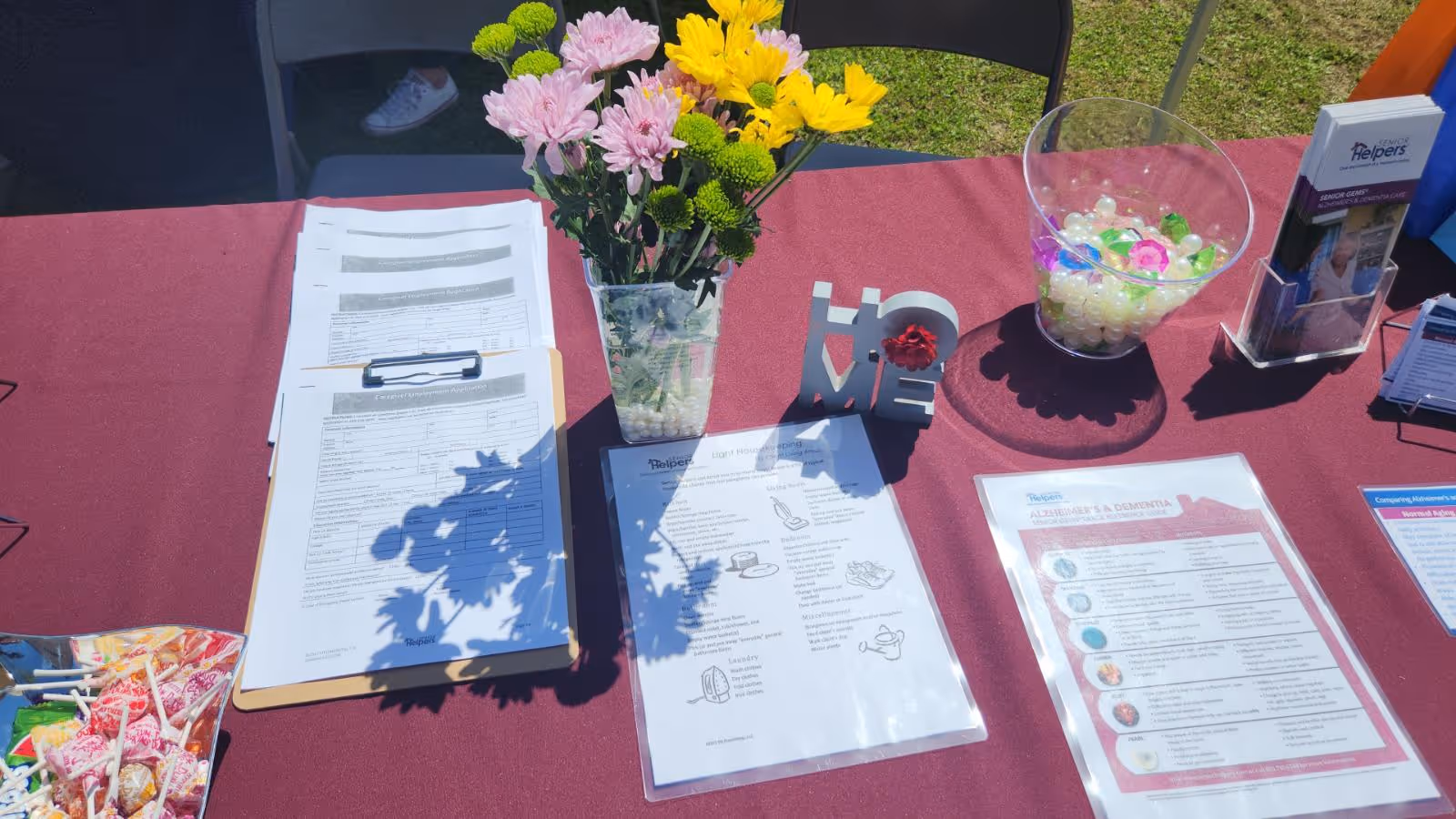 Outdoor information table for Senior Helpers with papers, a flower vase, and a bowl of candy.