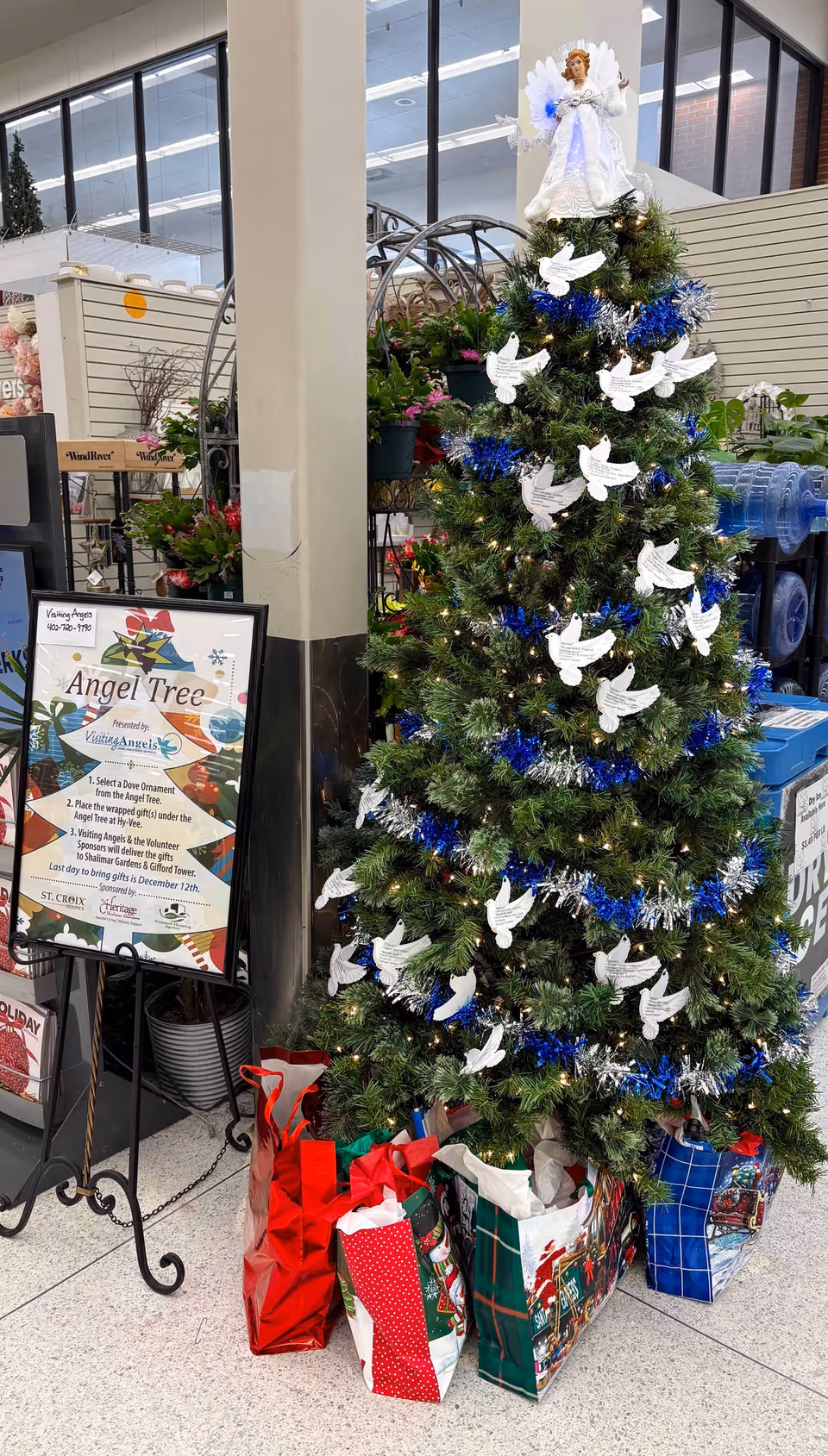 Decorated Christmas tree with angel ornaments and gift bags inside a facility lobby.