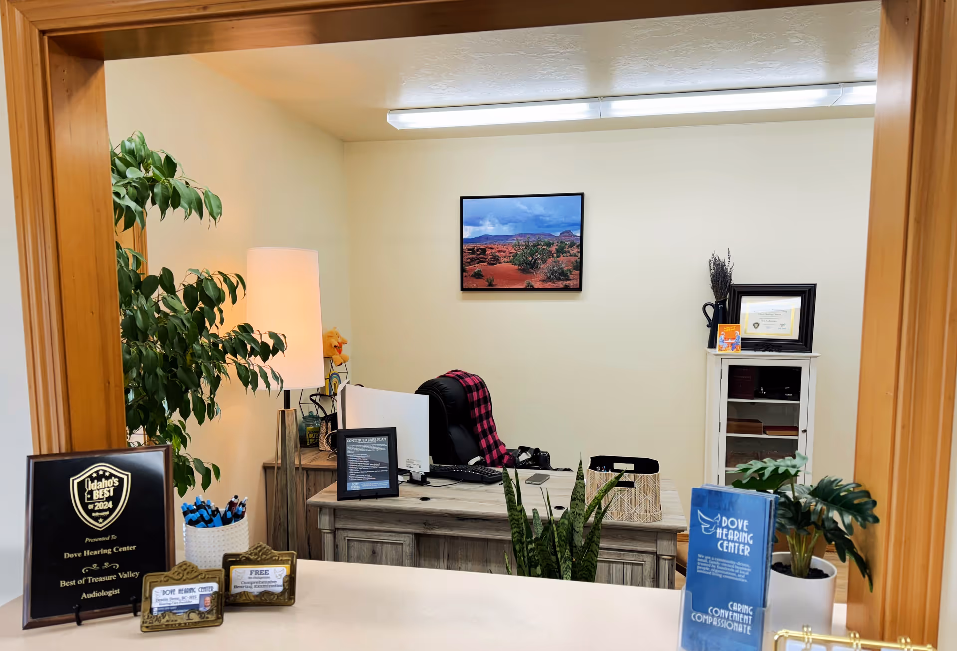 Reception area of Dove Hearing Center with desk, plants, certificate, and framed landscape photo.