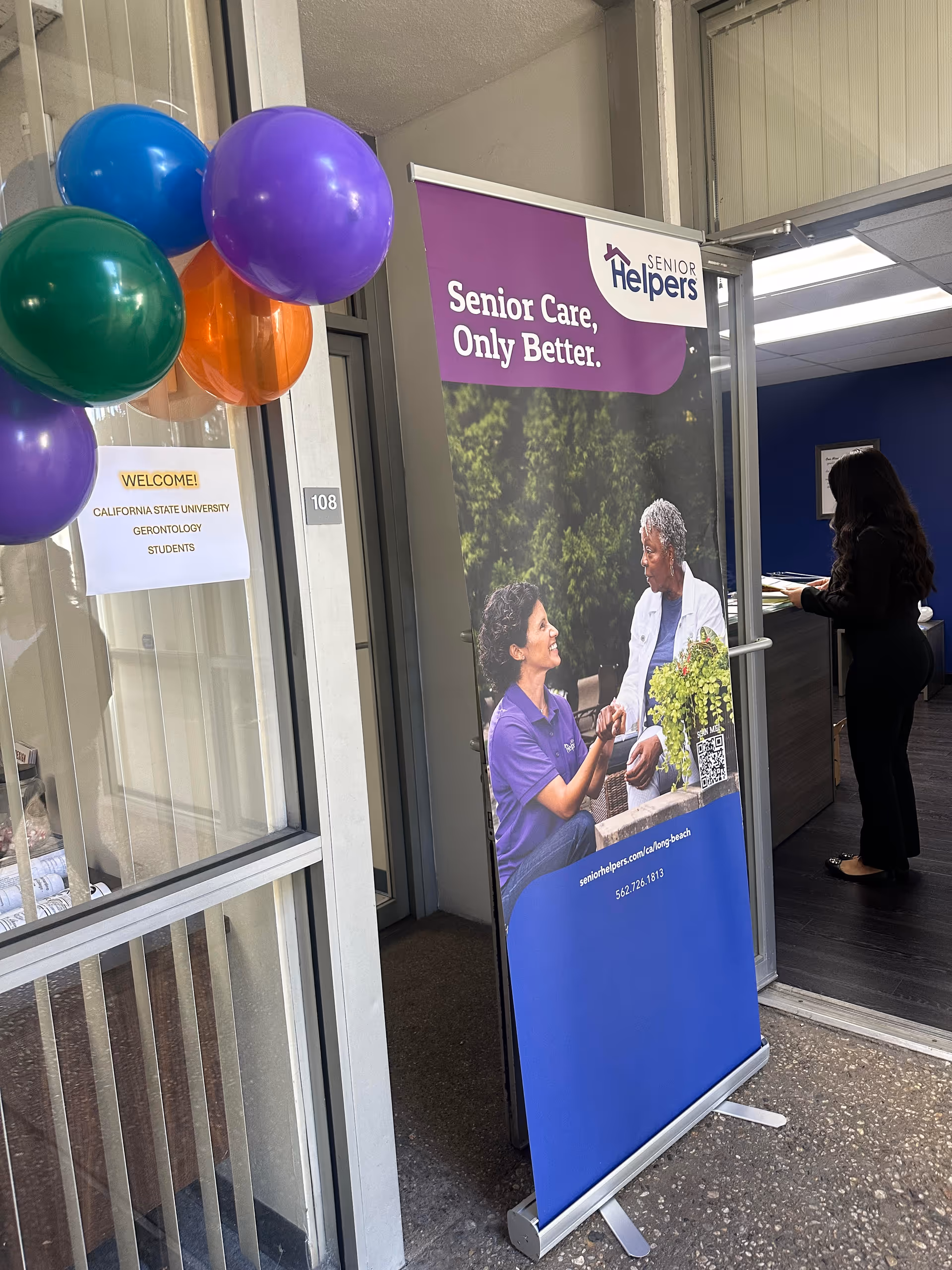 Entrance area of Senior Helpers of Long Beach with purple banner and balloons beside receptionist.