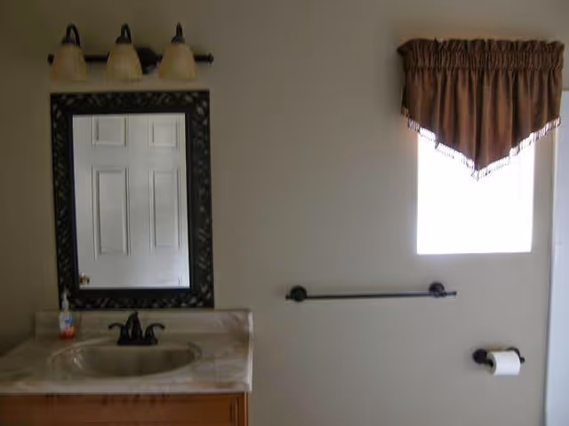Bathroom with sink, mirror, soap, towel bar, and small window.
